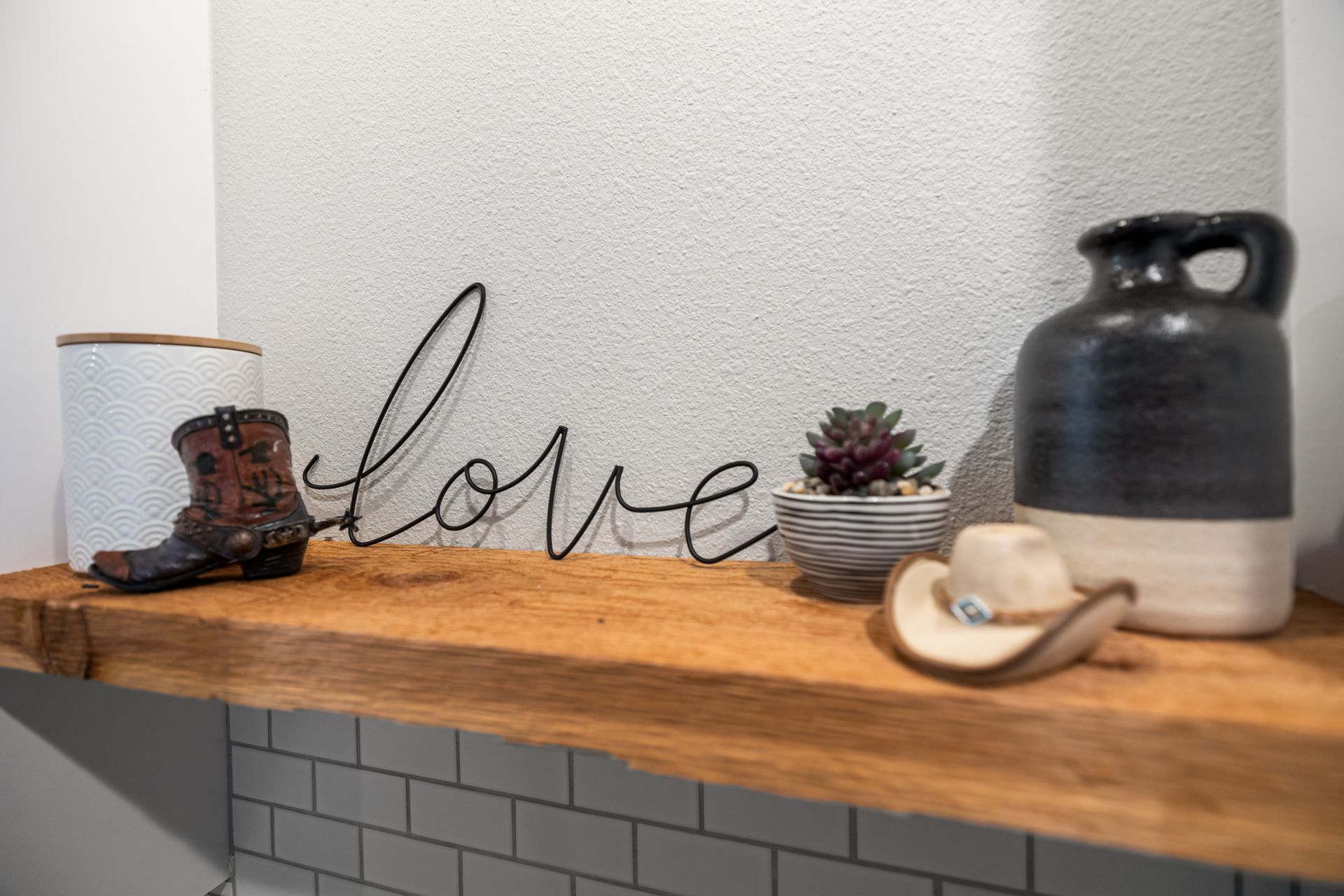 Decorative shelf with wire “love” sign, small boots, succulent, and ceramic kettle on a wood ledge