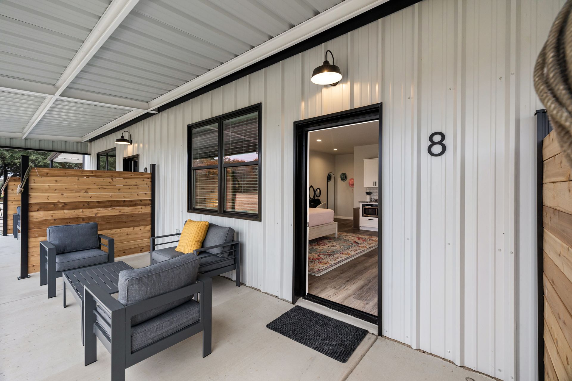 Covered porch with gray chairs, yellow pillow, and open door to a small room, house number 8 visible