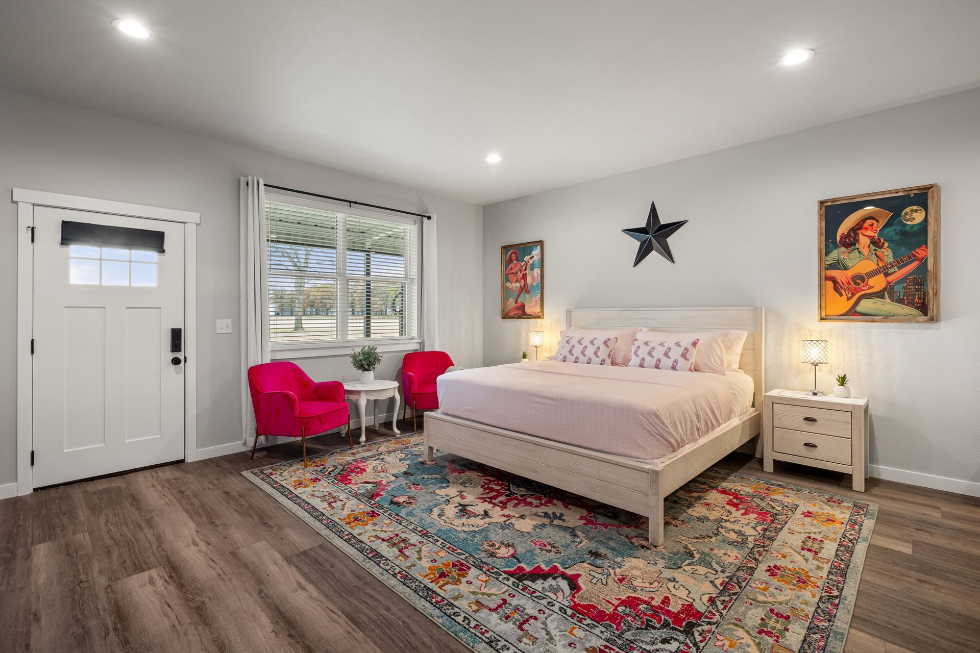Bright bedroom with white bed, colorful rug, pink chair, wall art, and wood floors