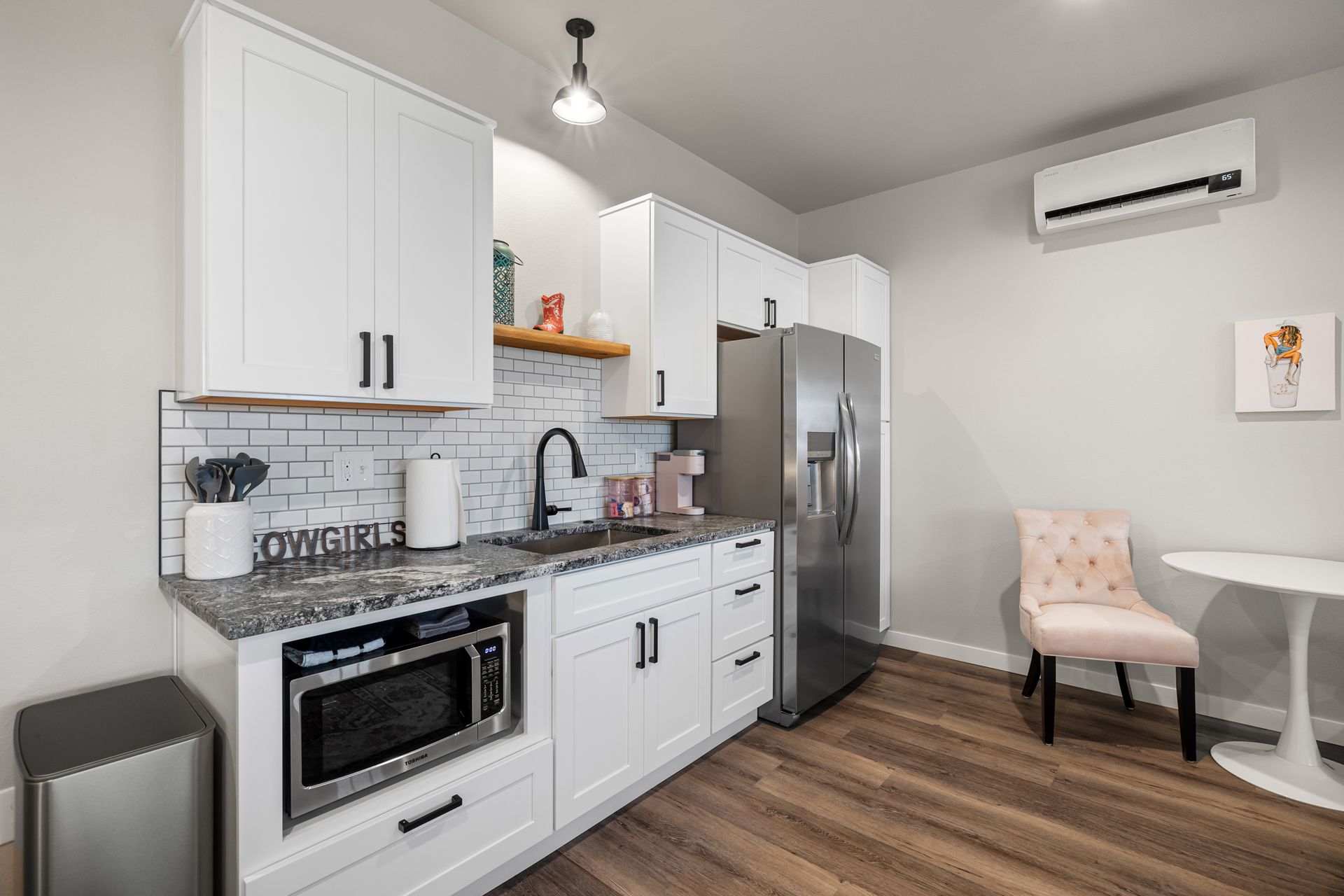 Modern white kitchen with stainless steel appliances, dark wood floors, and a small dining nook