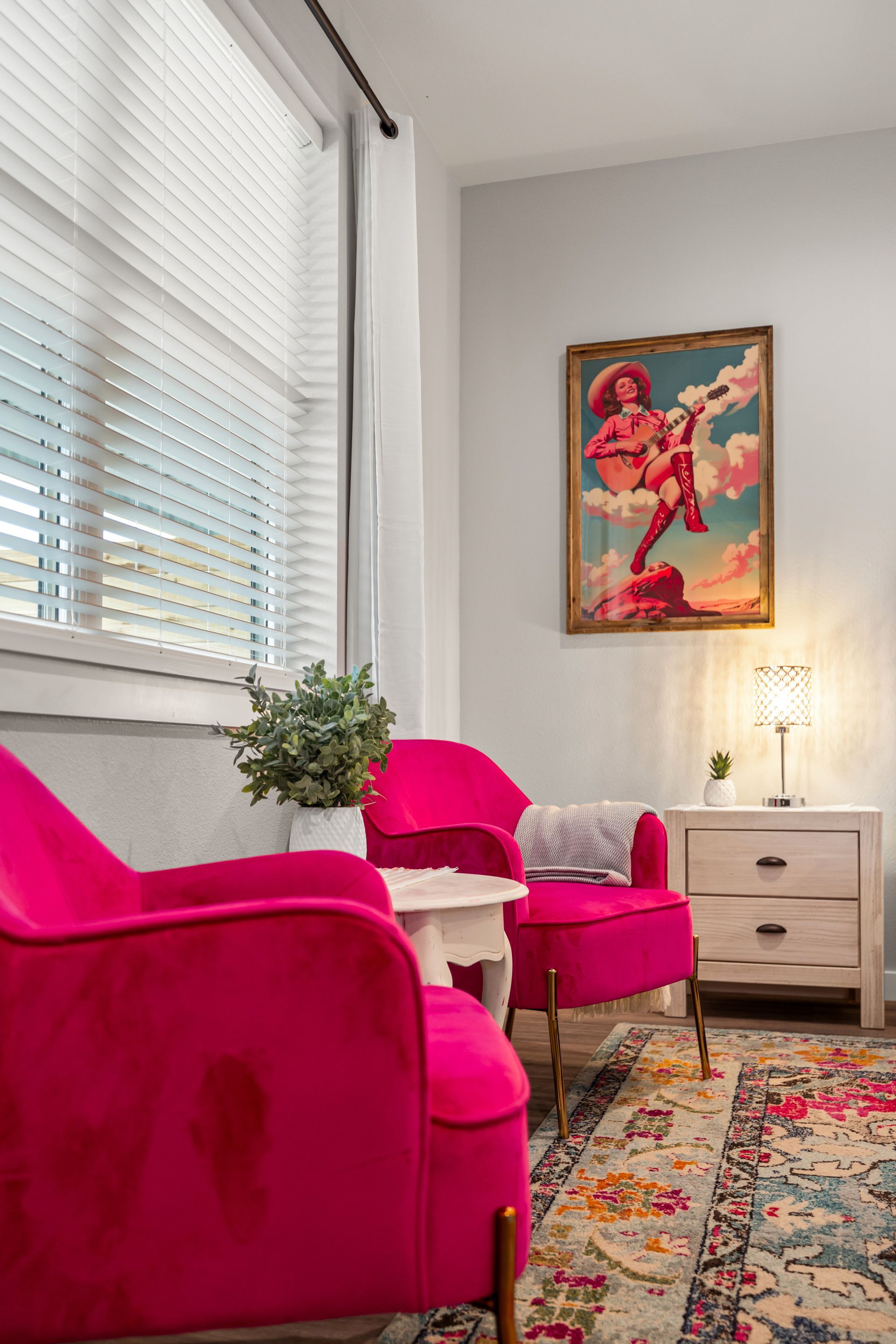 Bright living room with hot pink chairs, a patterned rug, a small table, and colorful wall art
