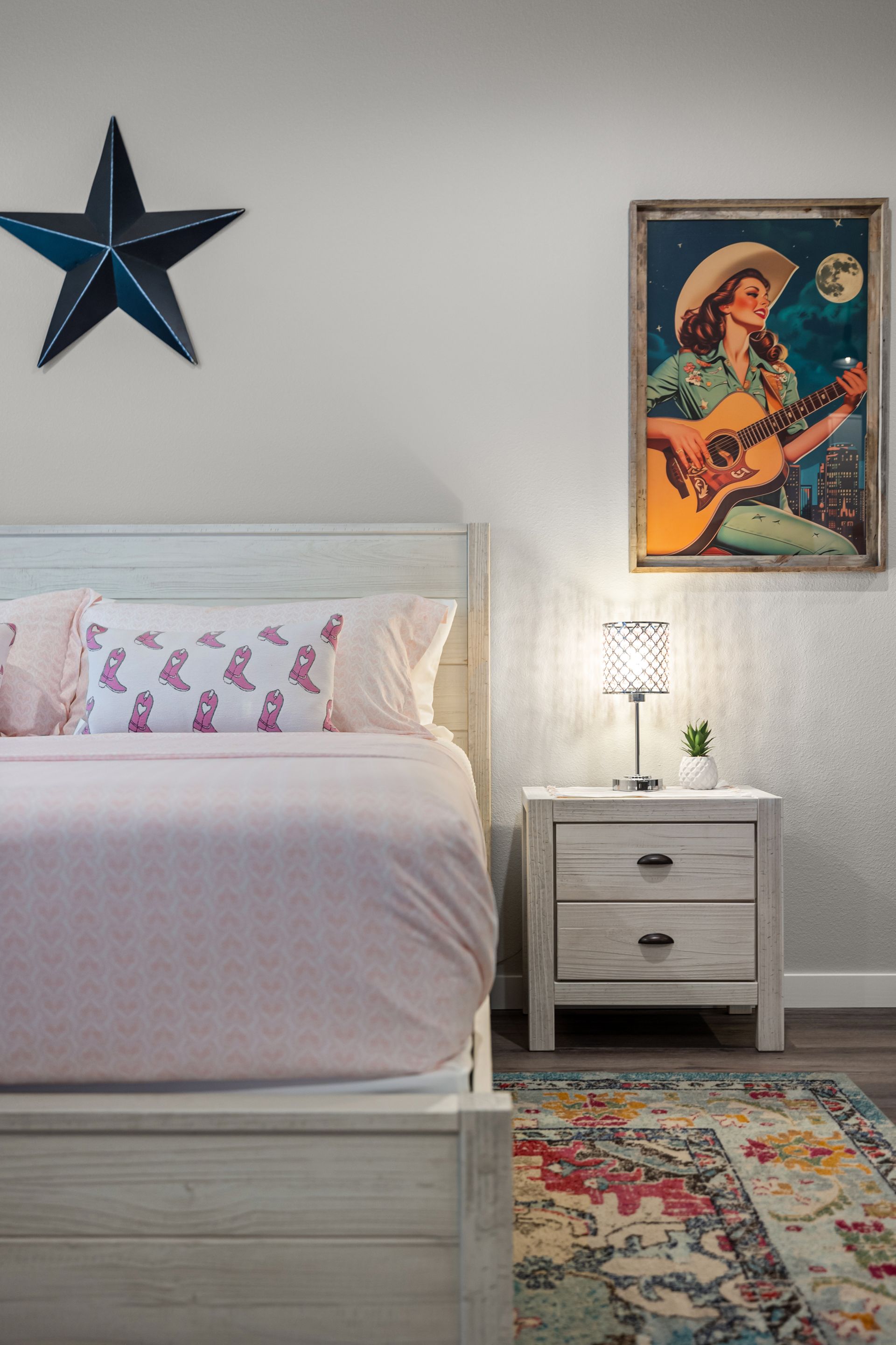 A cozy bedroom with a white bed, star wall decor, colorful rug, and nightstand beside a framed guitar poster