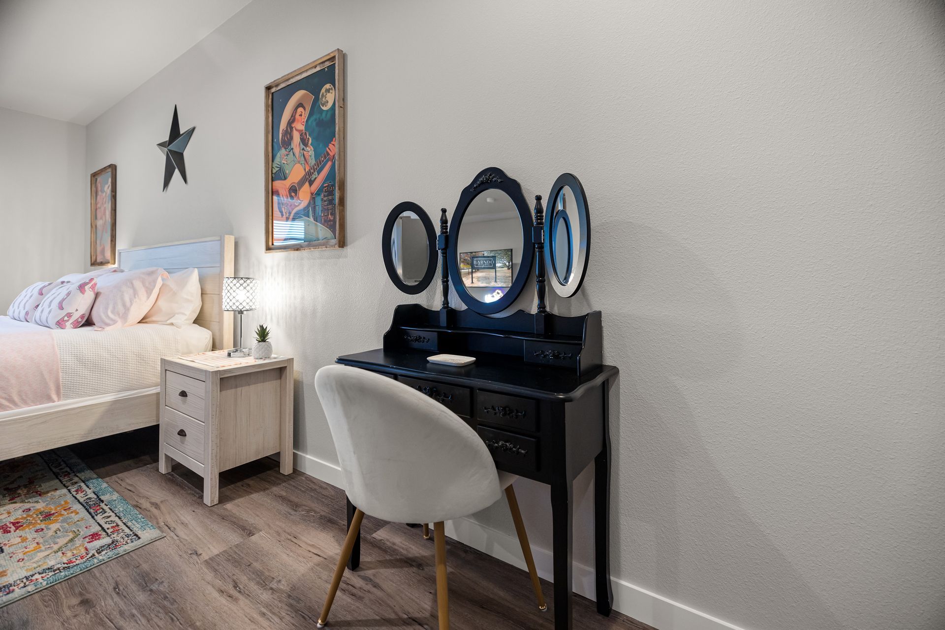 Bedroom vanity with round mirror, black desk, white chair, bed, and wall art on gray walls