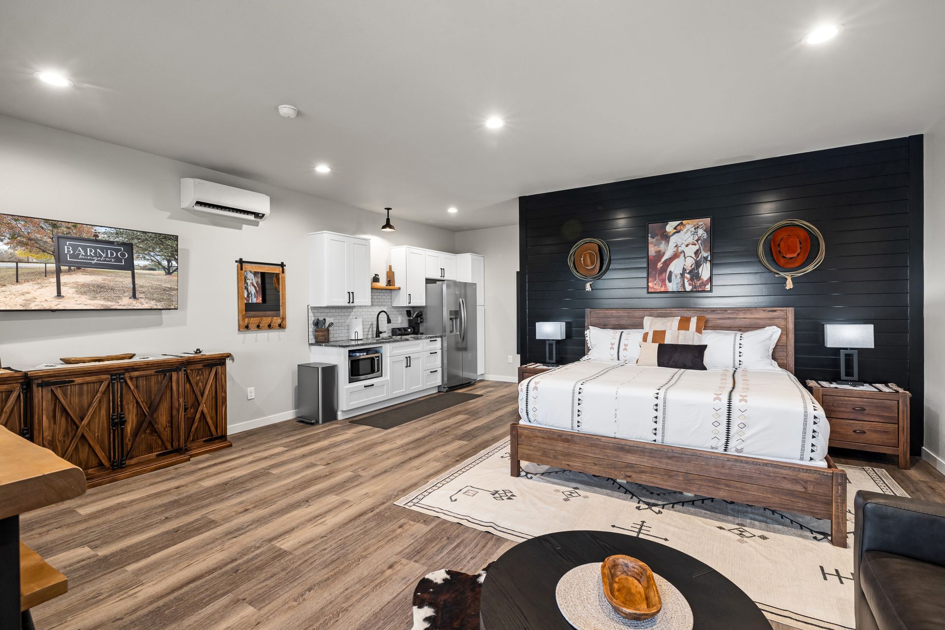 Modern bedroom with wood bed, dark accent wall, kitchenette, and cozy seating area
