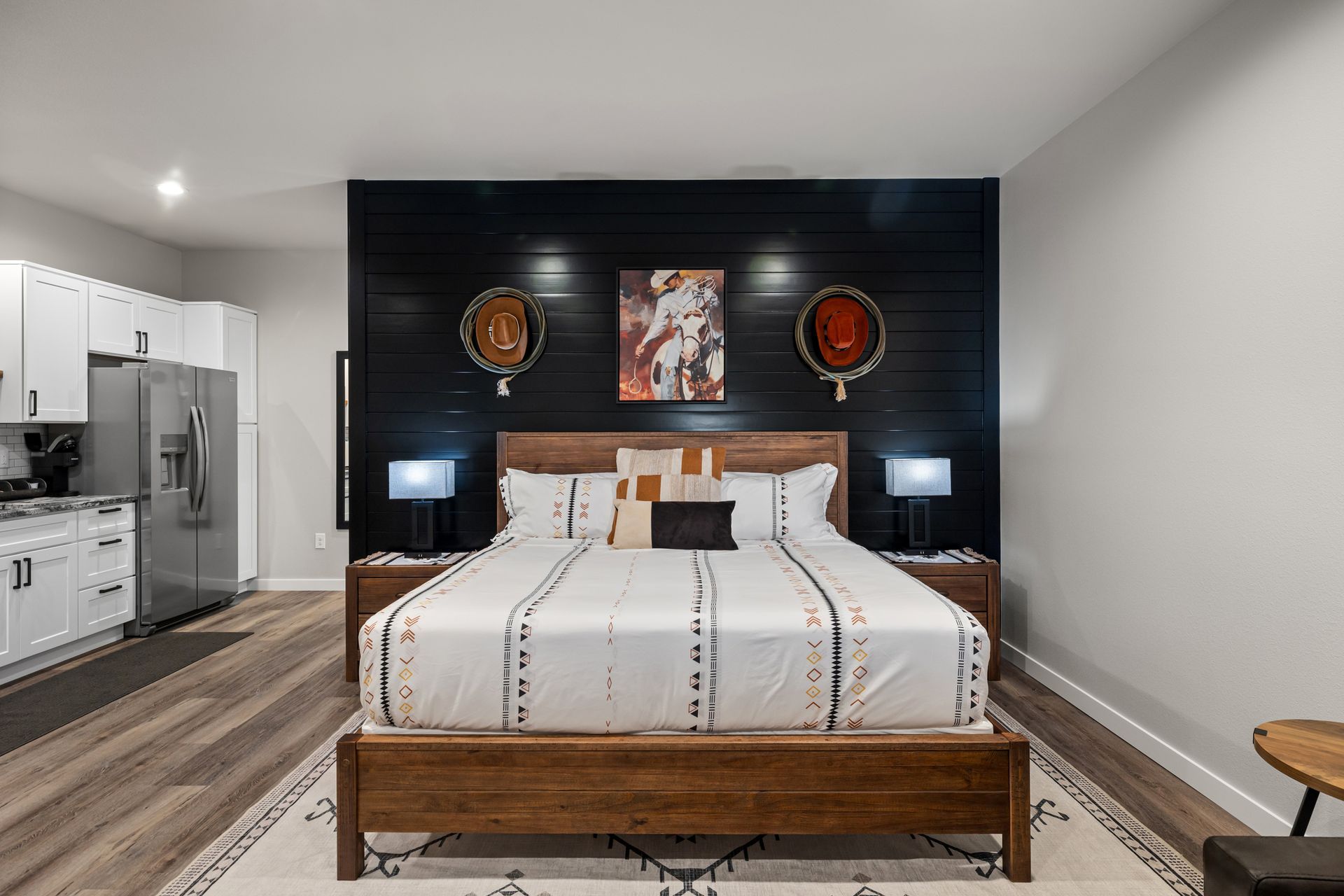 Modern bedroom with a wooden bed, black accent wall, bedside lamps, and a stainless steel refrigerator.