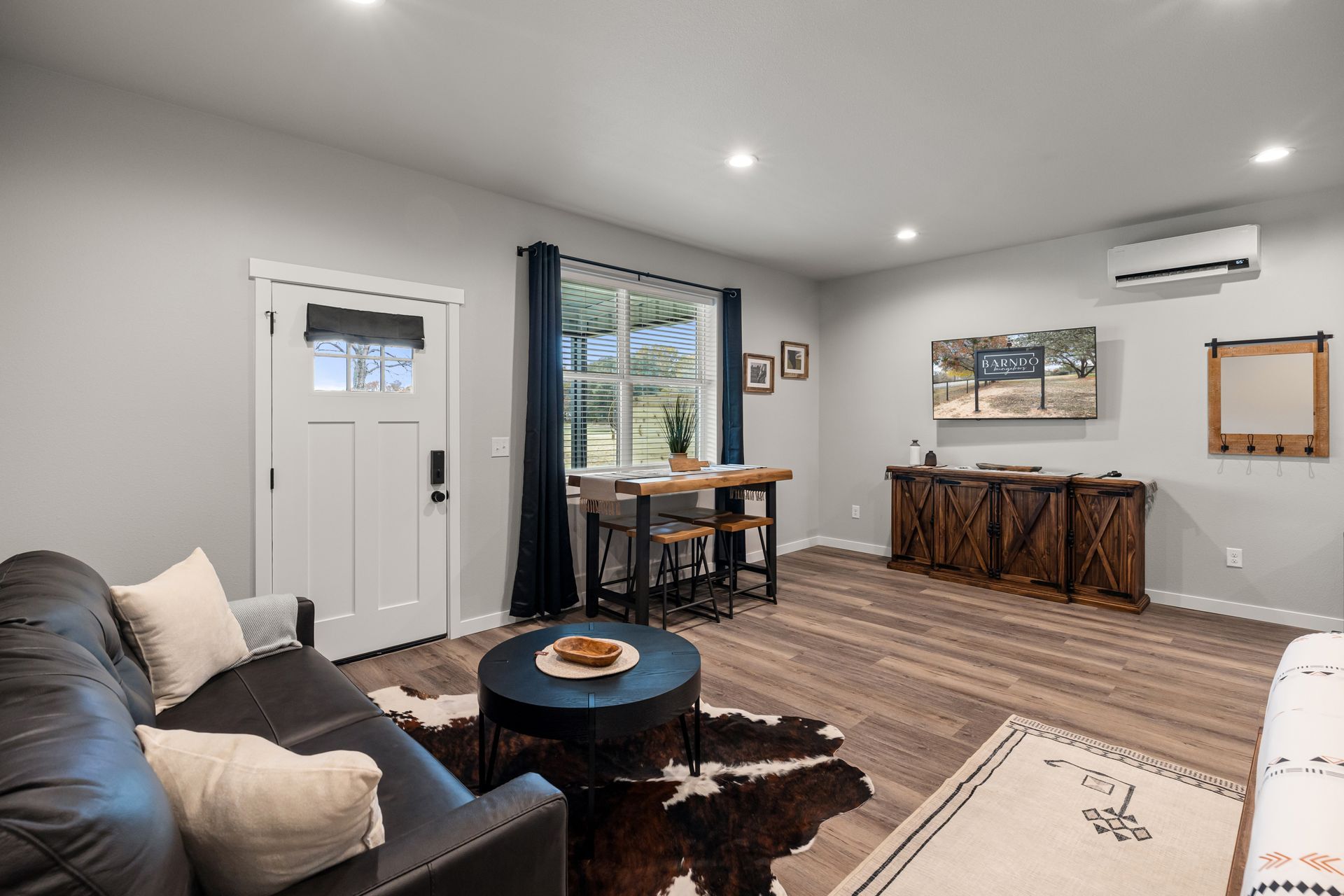 Modern gray living room with black sofa, round coffee table, dining nook, and wall art