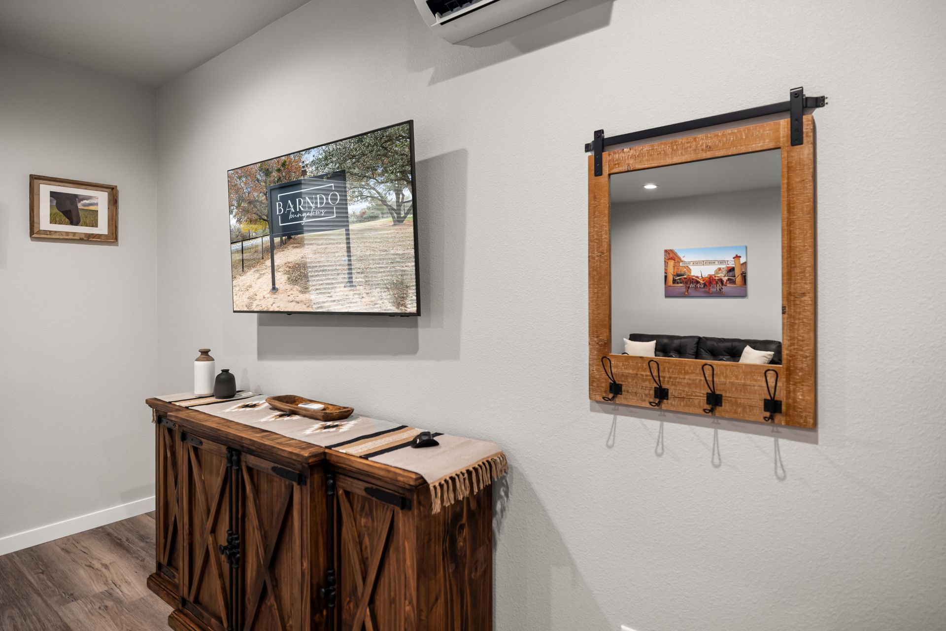 Minimalist room with wall-mounted TV, wooden console, and framed mirror above a bench with hooks.