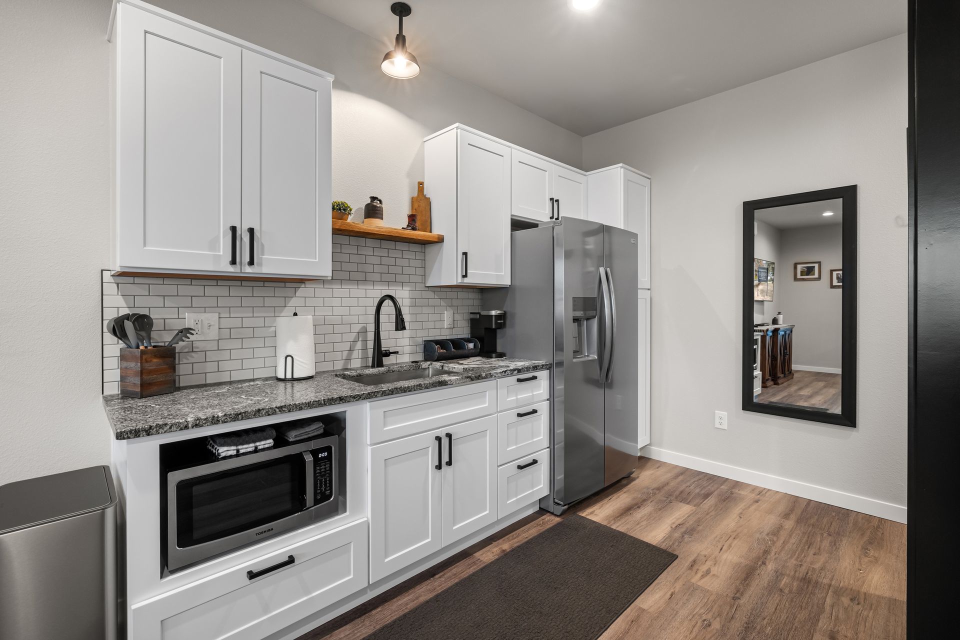 Modern white kitchen with stainless steel appliances, gray tile backsplash, and wood flooring