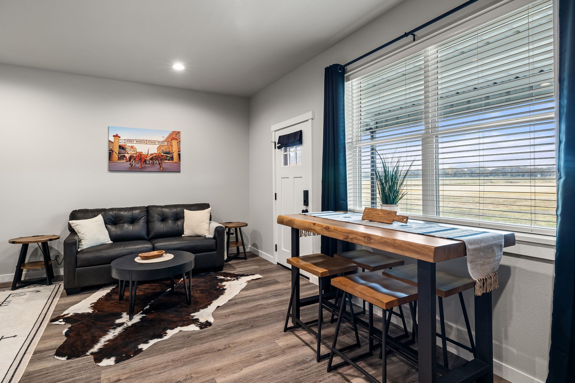 Bright living room with gray sofa, cowhide rug, and a dining table by large windows.