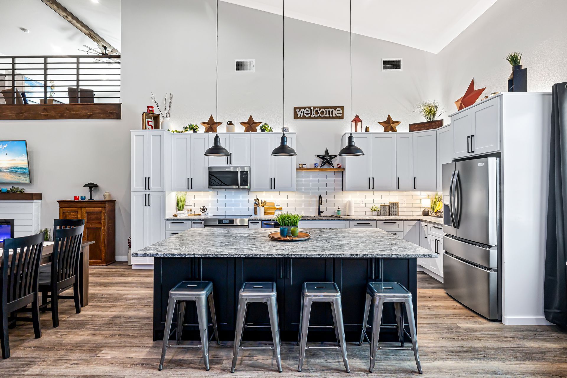 Modern kitchen with gray cabinets, stainless appliances, granite island, and four metal stools