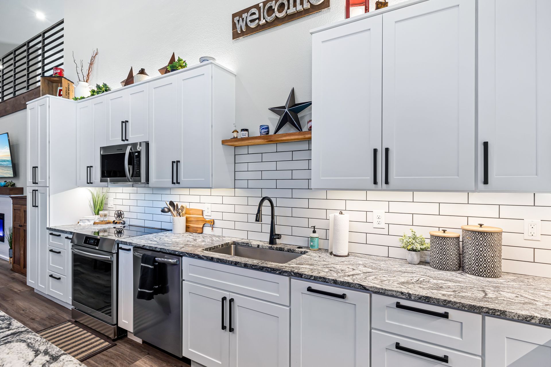 Modern kitchen showroom with white cabinets, stainless steel appliances, and granite countertops