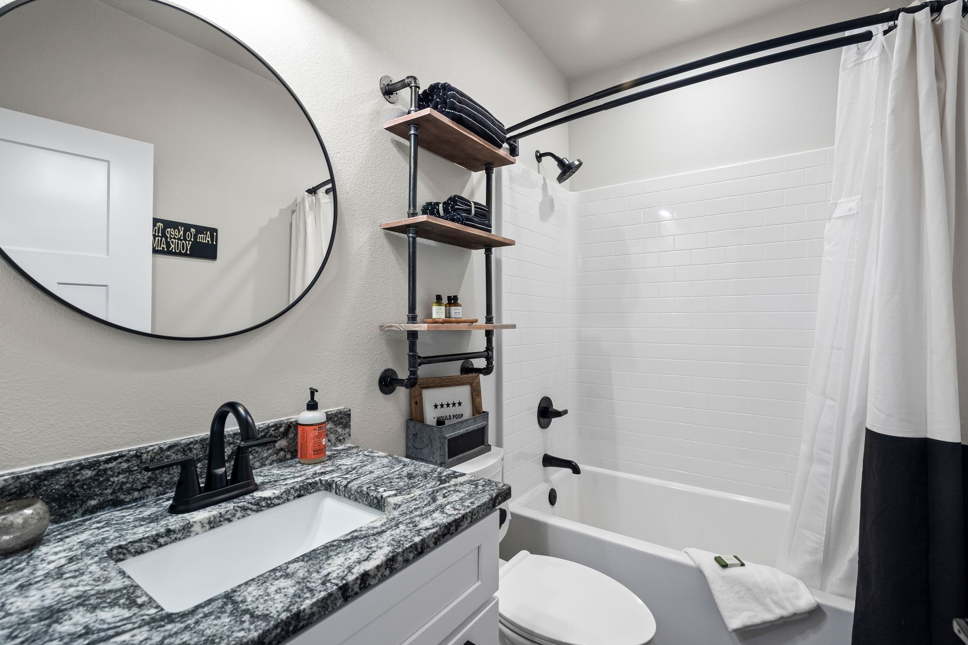 Modern bathroom with granite vanity, round mirror, bathtub with shower curtain, and wall shelves