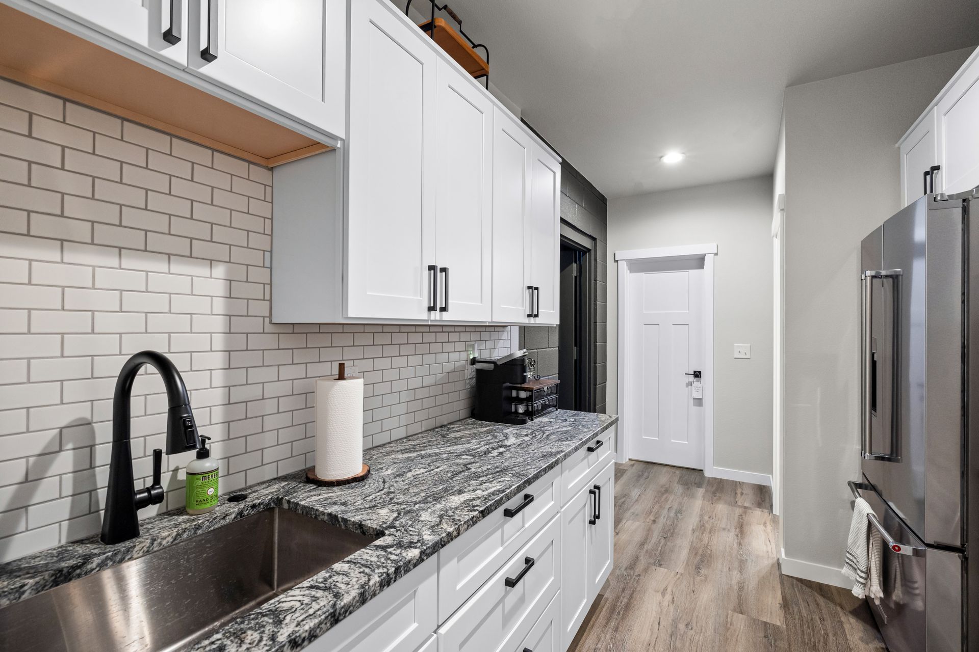 Bright modern galley kitchen with white cabinets, granite counters, subway tile, and stainless steel appliances
