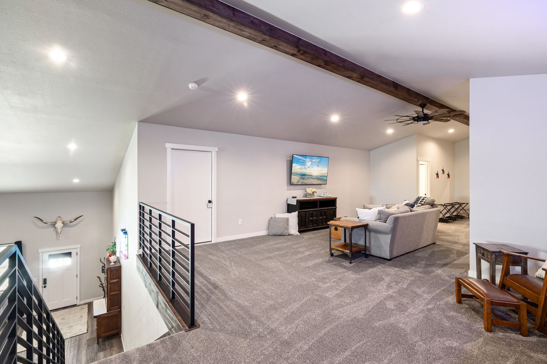 Open-concept living room with gray carpet, sectional sofa, TV, and loft railing under vaulted ceiling