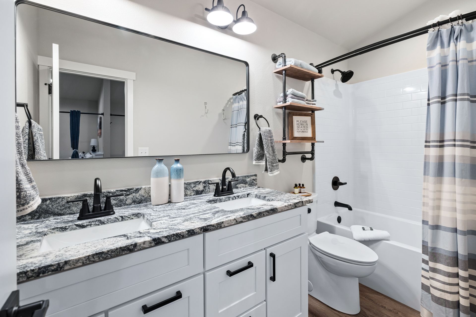 Bright bathroom with marble vanity, large mirror, toilet, and white tub with blue shower curtain.