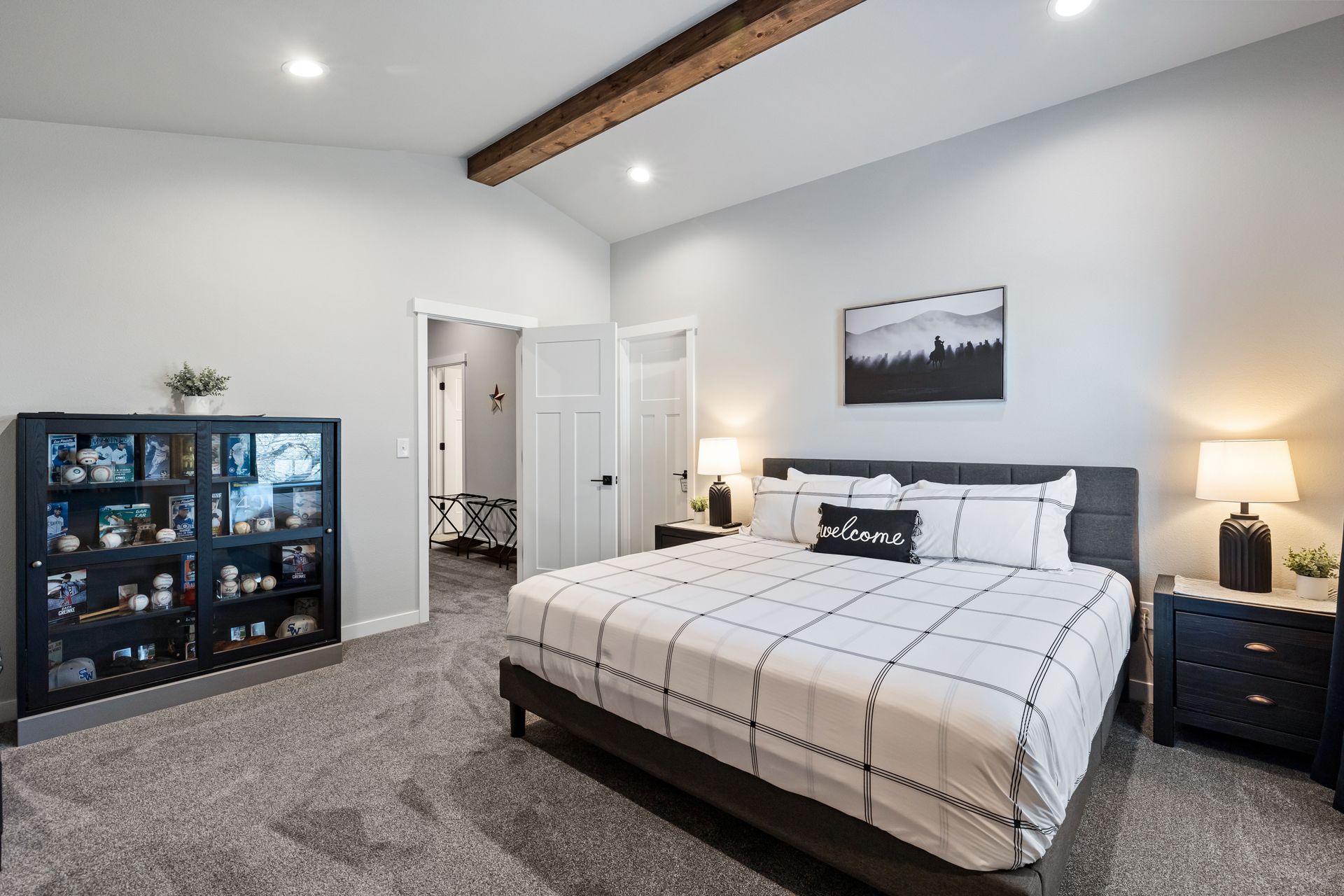 Bright modern bedroom with a bed, nightstands, dresser, carpet, and vaulted ceiling with wood beam