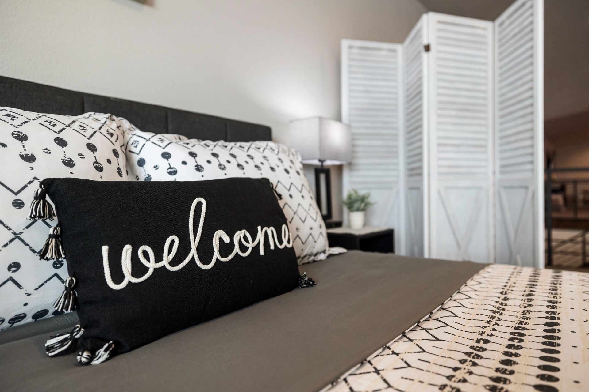 Bedroom with black-and-white bedding and a black “welcome” pillow on the bed