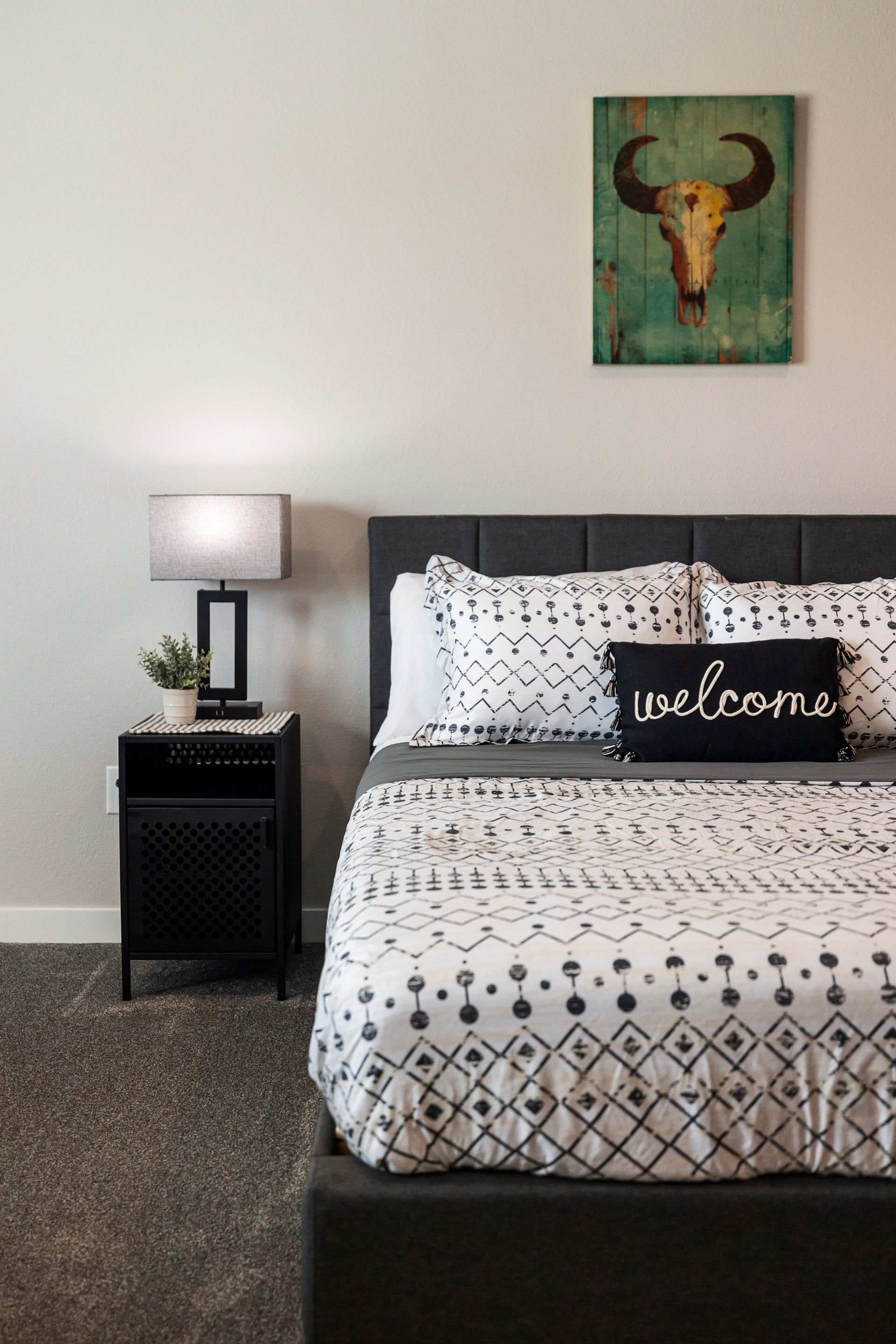 Neat bedroom with a dark bed, patterned bedding, bedside lamp, and bull wall art.