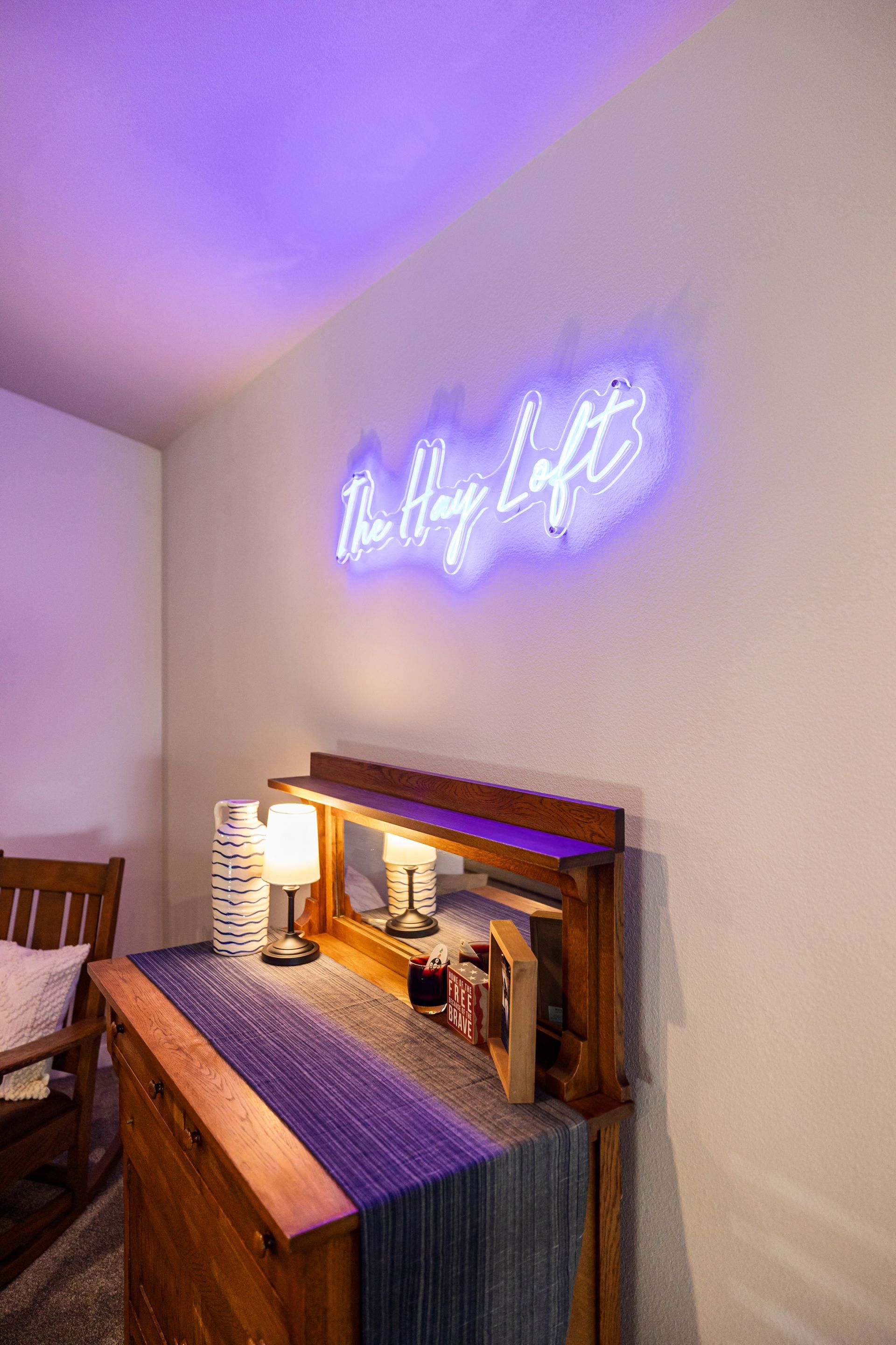 Neon sign above a wooden dresser in a softly lit room with purple accent lighting.