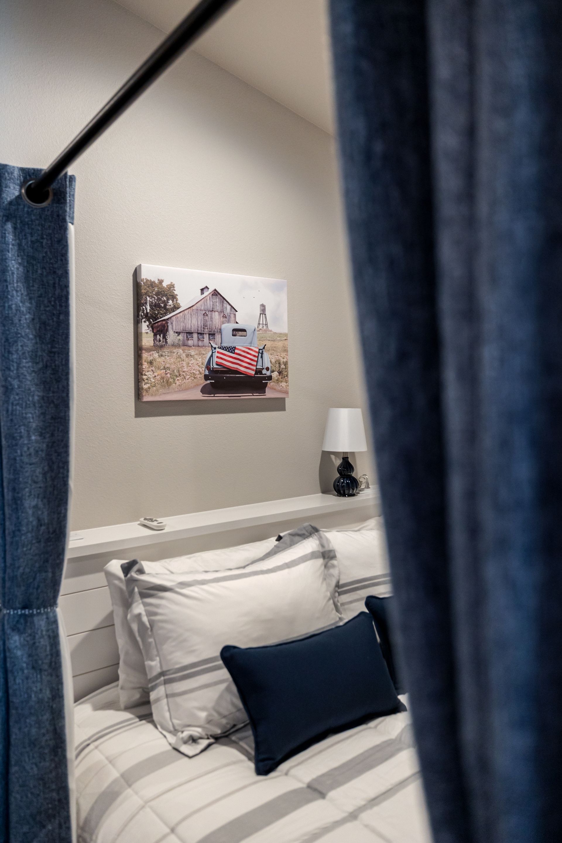 Cozy bedroom with a white bed, blue pillows, and dark curtains framing the view.