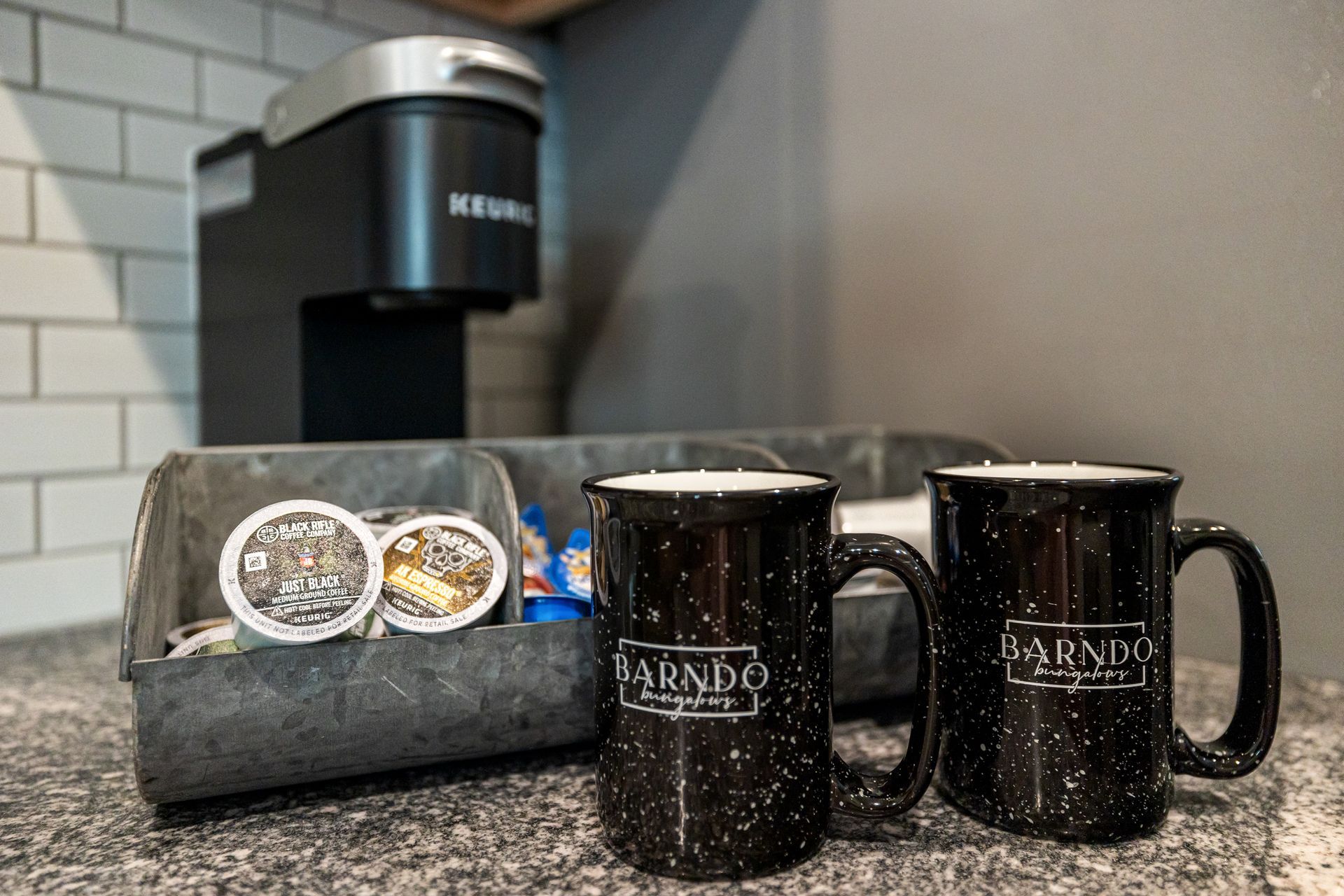 Two black mugs beside a coffee bag with coffee beans on a kitchen countertop