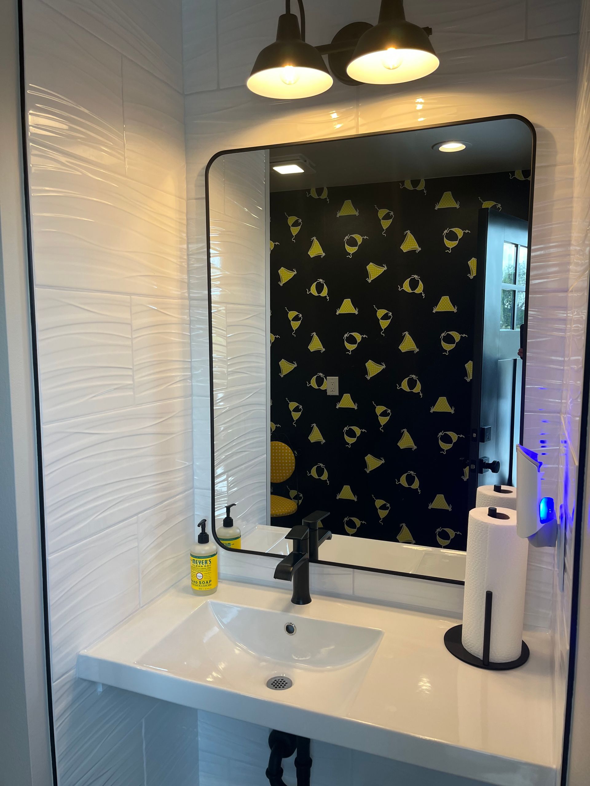 Bathroom sink and mirror with black wallpaper and overhead lights