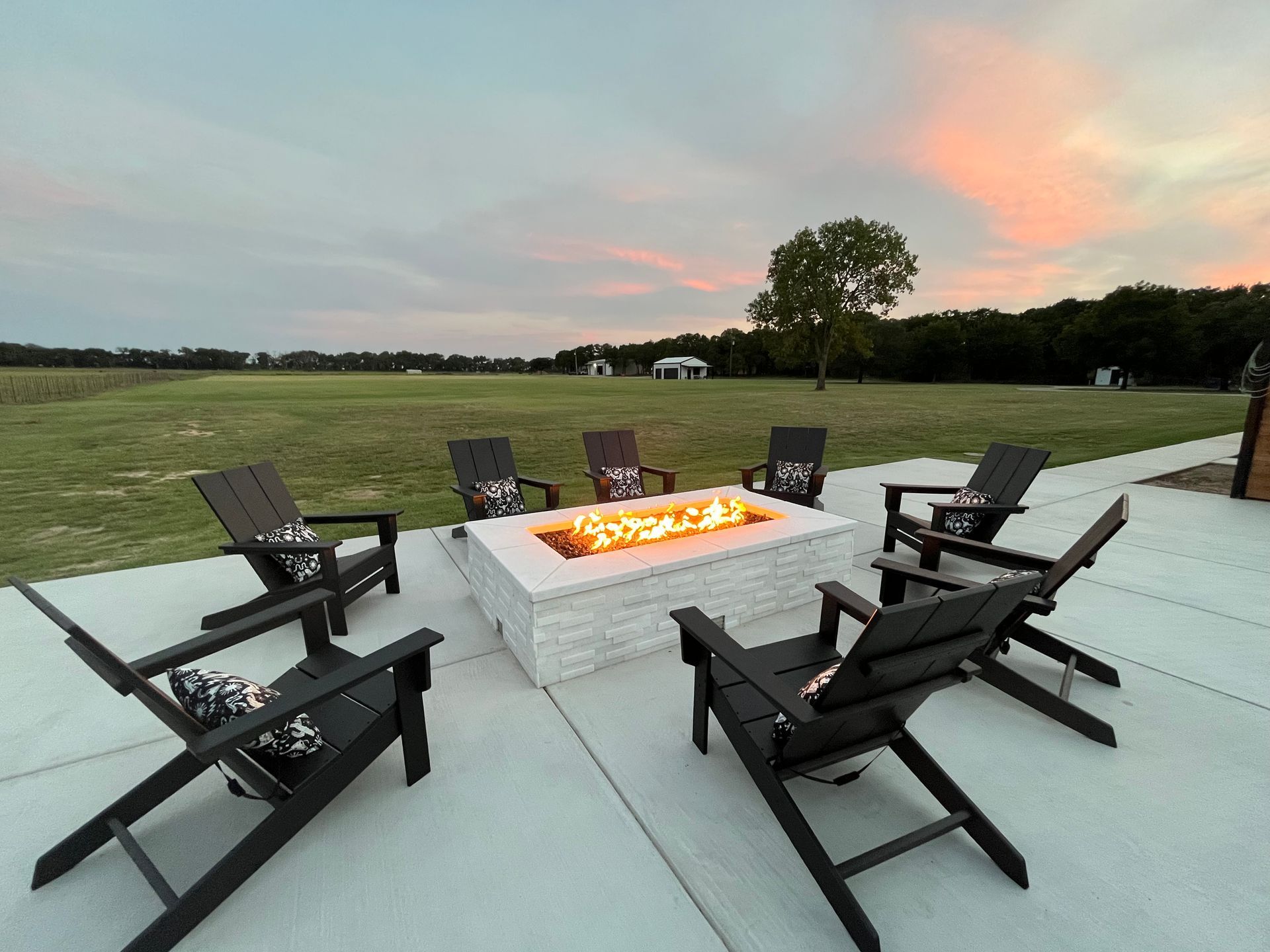Patio fire pit surrounded by black chairs at sunset in an open field