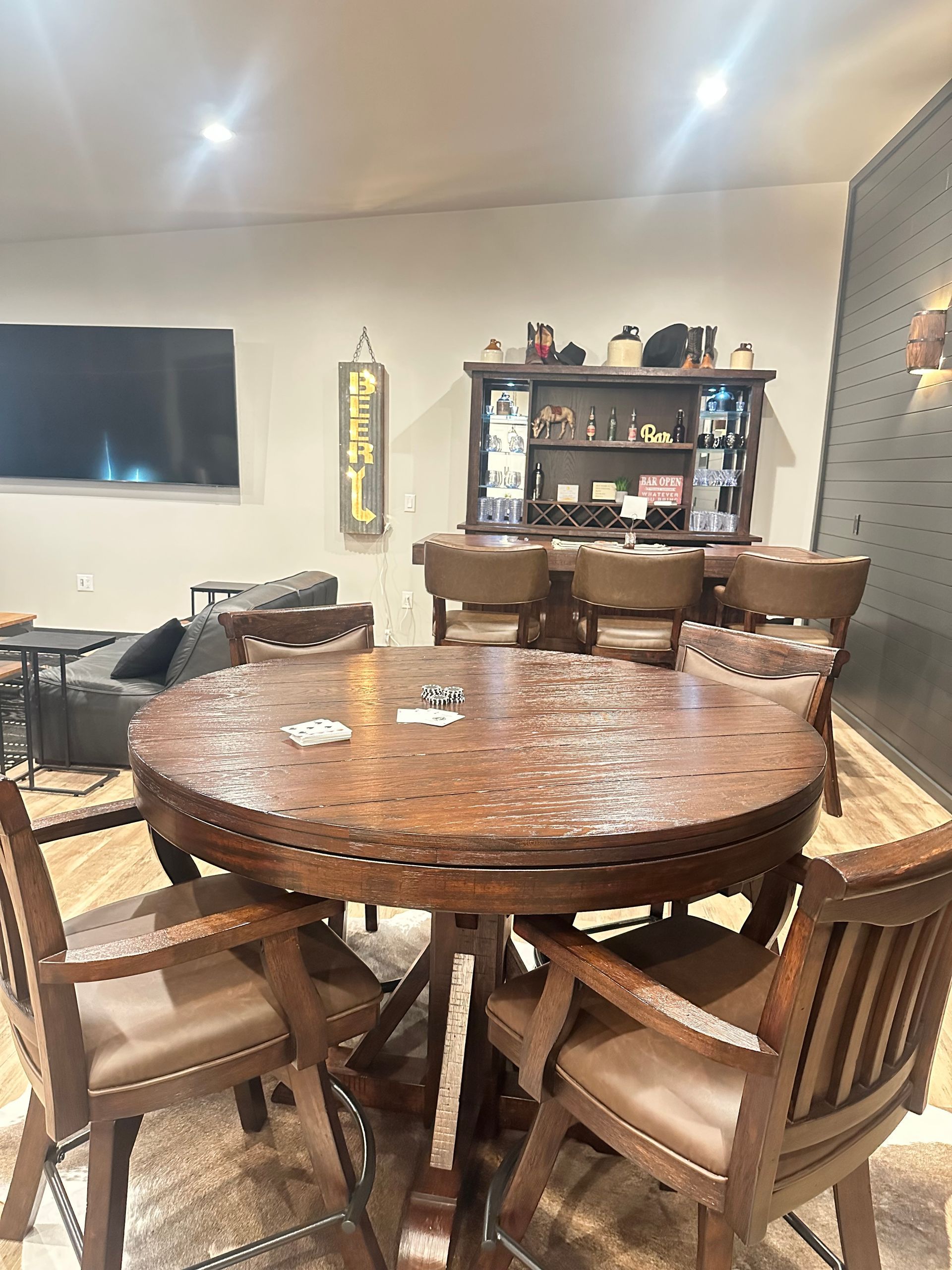 Round wooden dining table with chairs in a warmly lit room and a bar cabinet in the background