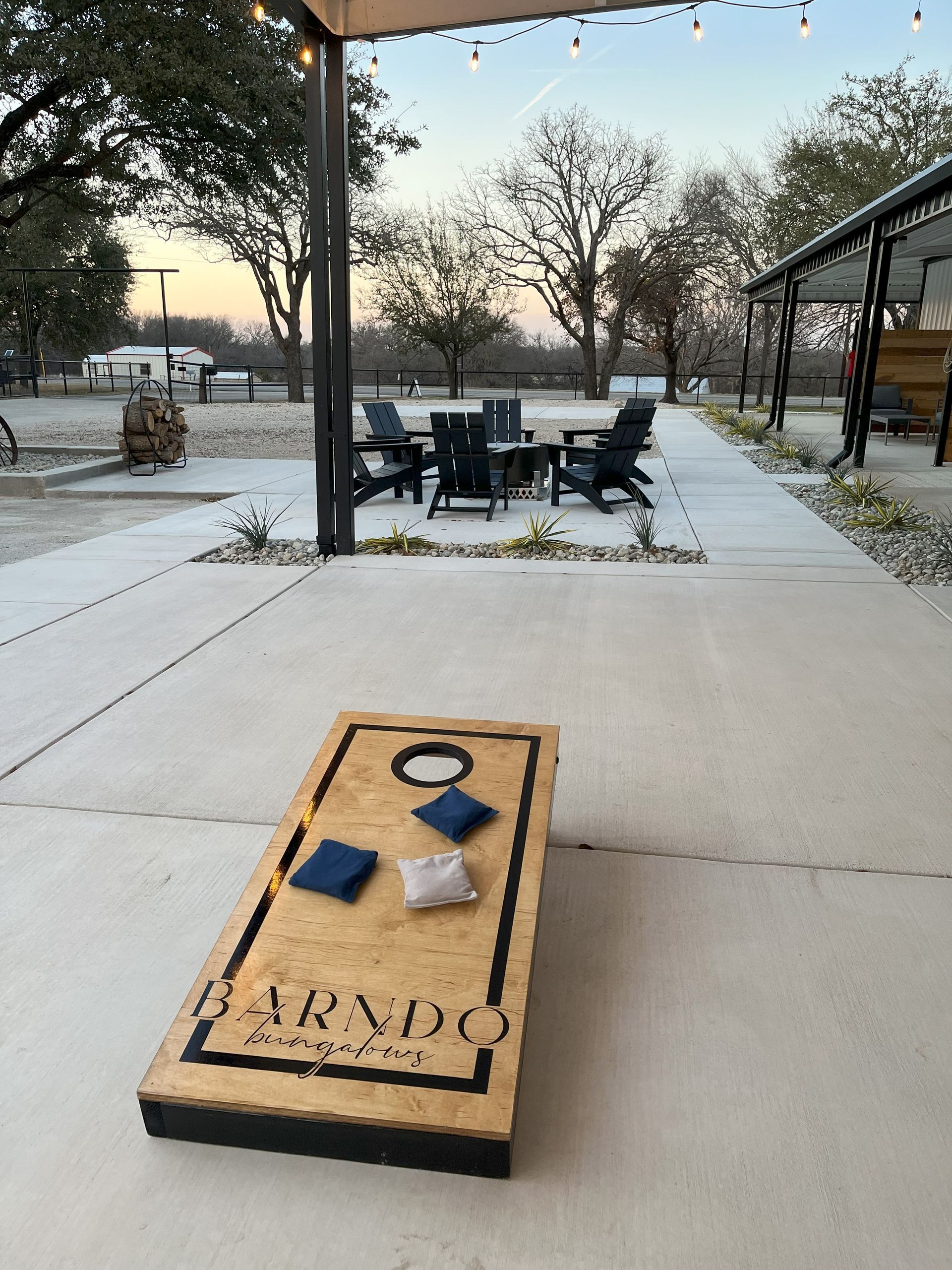 Cornhole board with bean bags on a snowy patio beside outdoor café tables and chairs