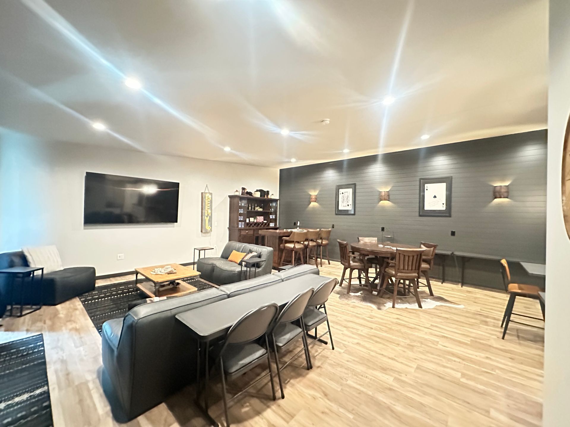 Modern lounge with gray sofa, wall-mounted TV, tables, chairs, and warm pendant lighting