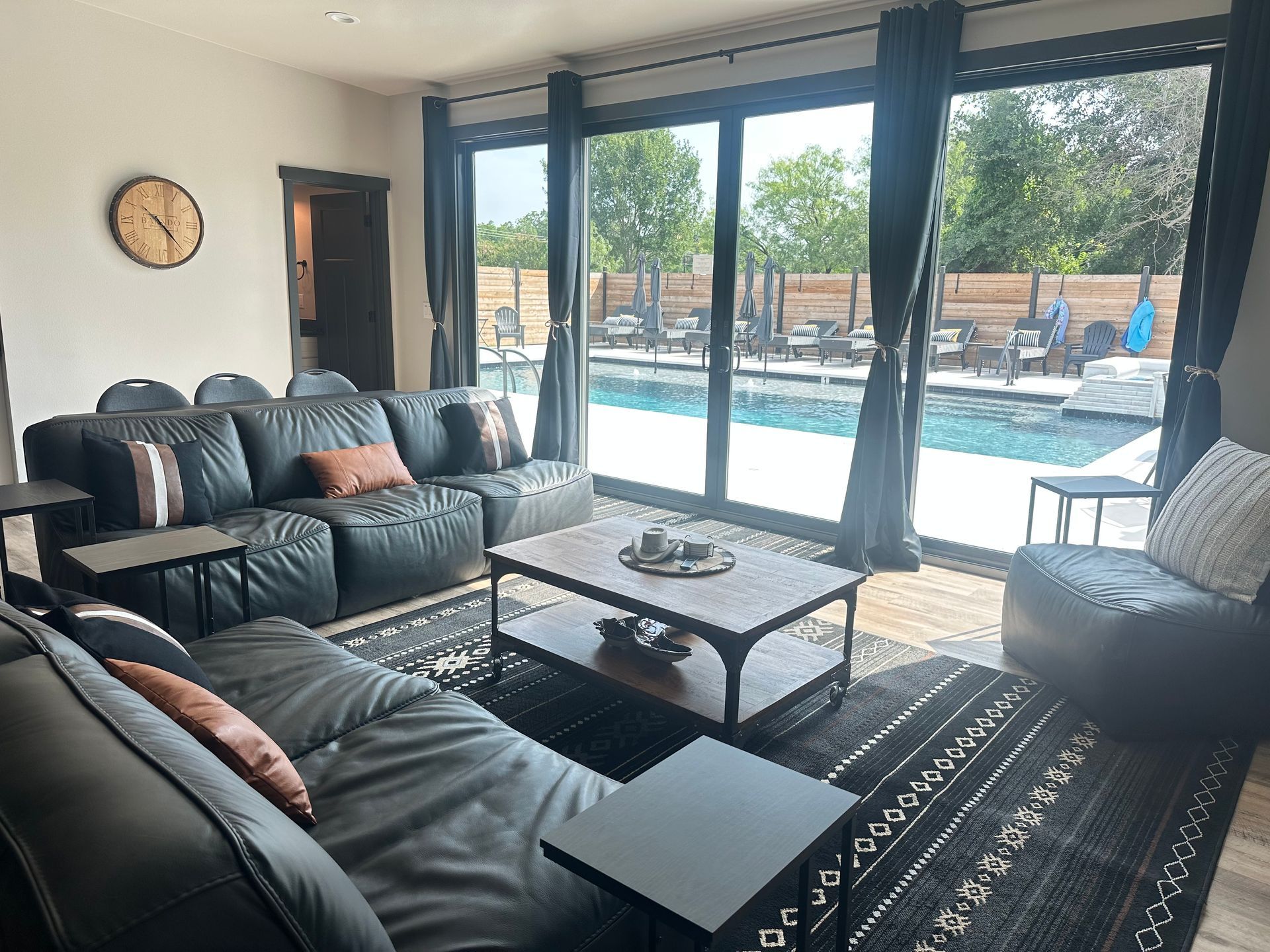 Modern living room with gray sectional, coffee table, and large sliding doors overlooking a backyard pool.