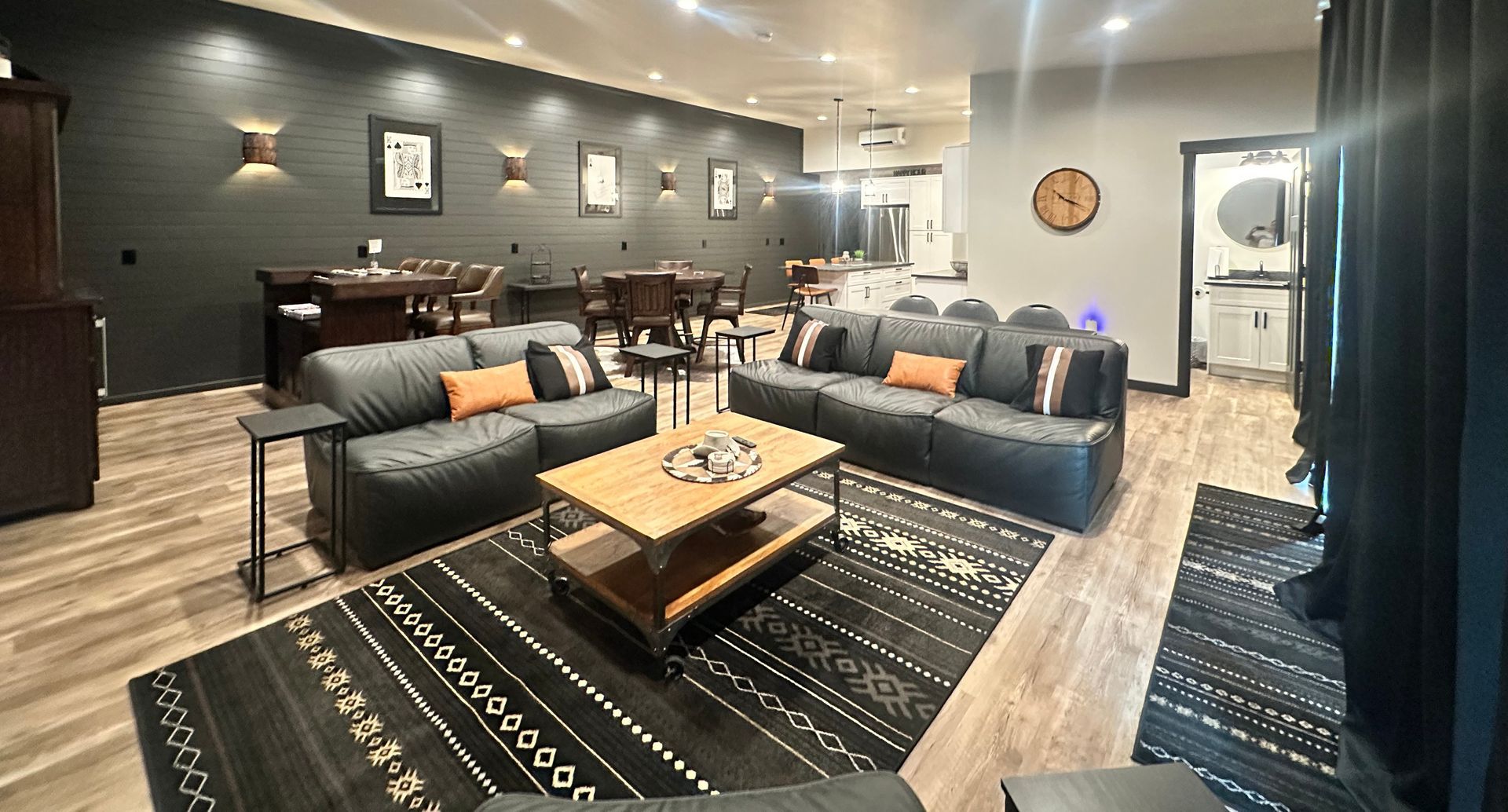 Modern living room with black sofas, wood coffee table, patterned rugs, and wall art under warm lighting