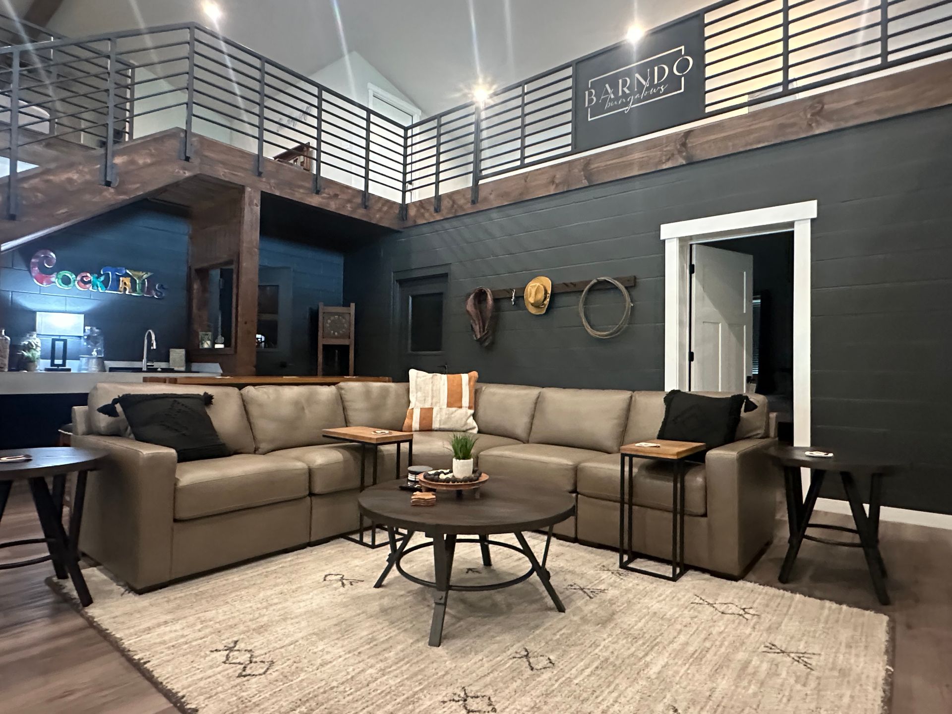 Modern lounge with brown sectional sofa, coffee tables, rug, and loft railing in a brick-and-wood interior