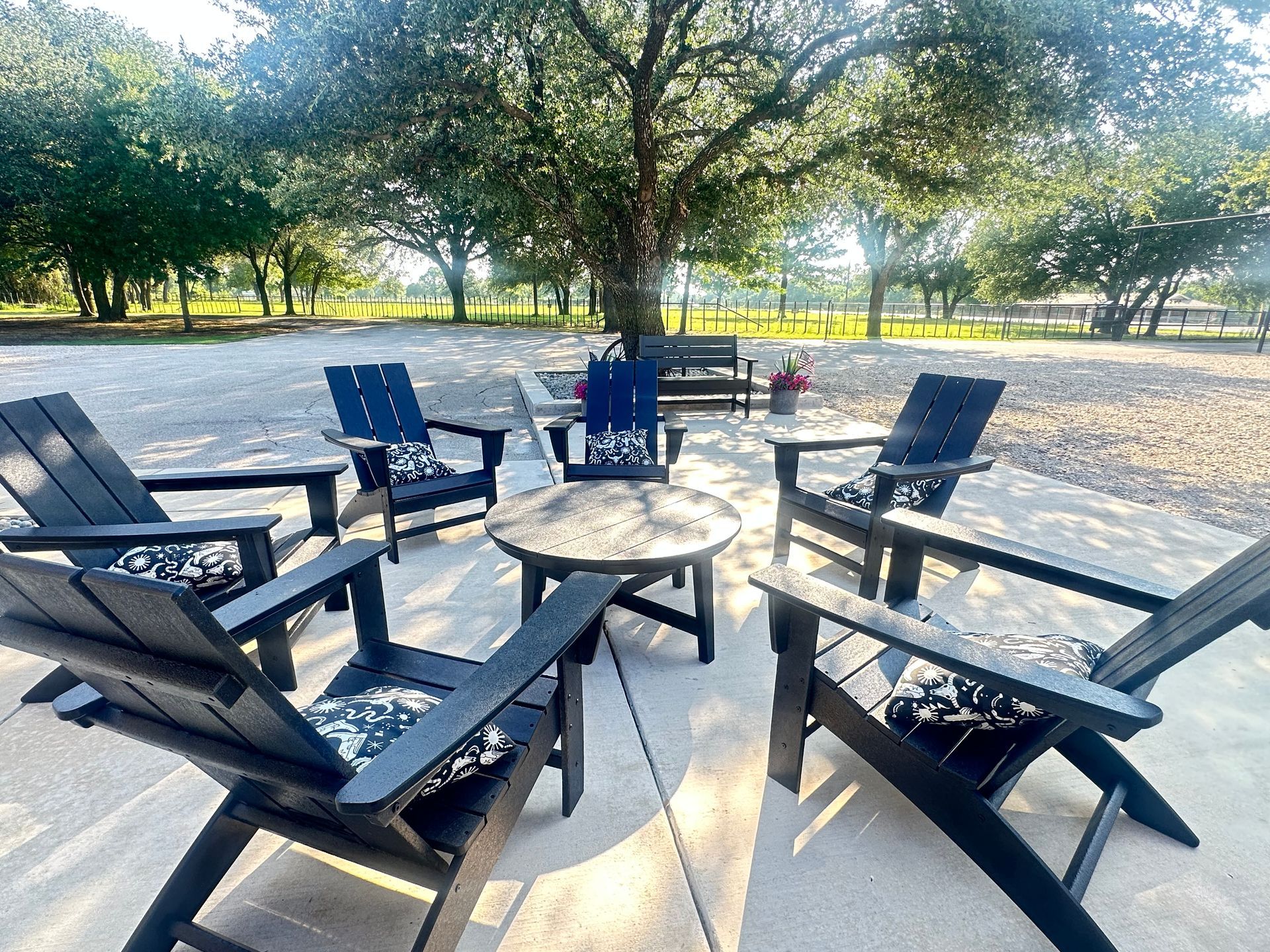 Outdoor seating area with black chairs around a round table under a tree in a park