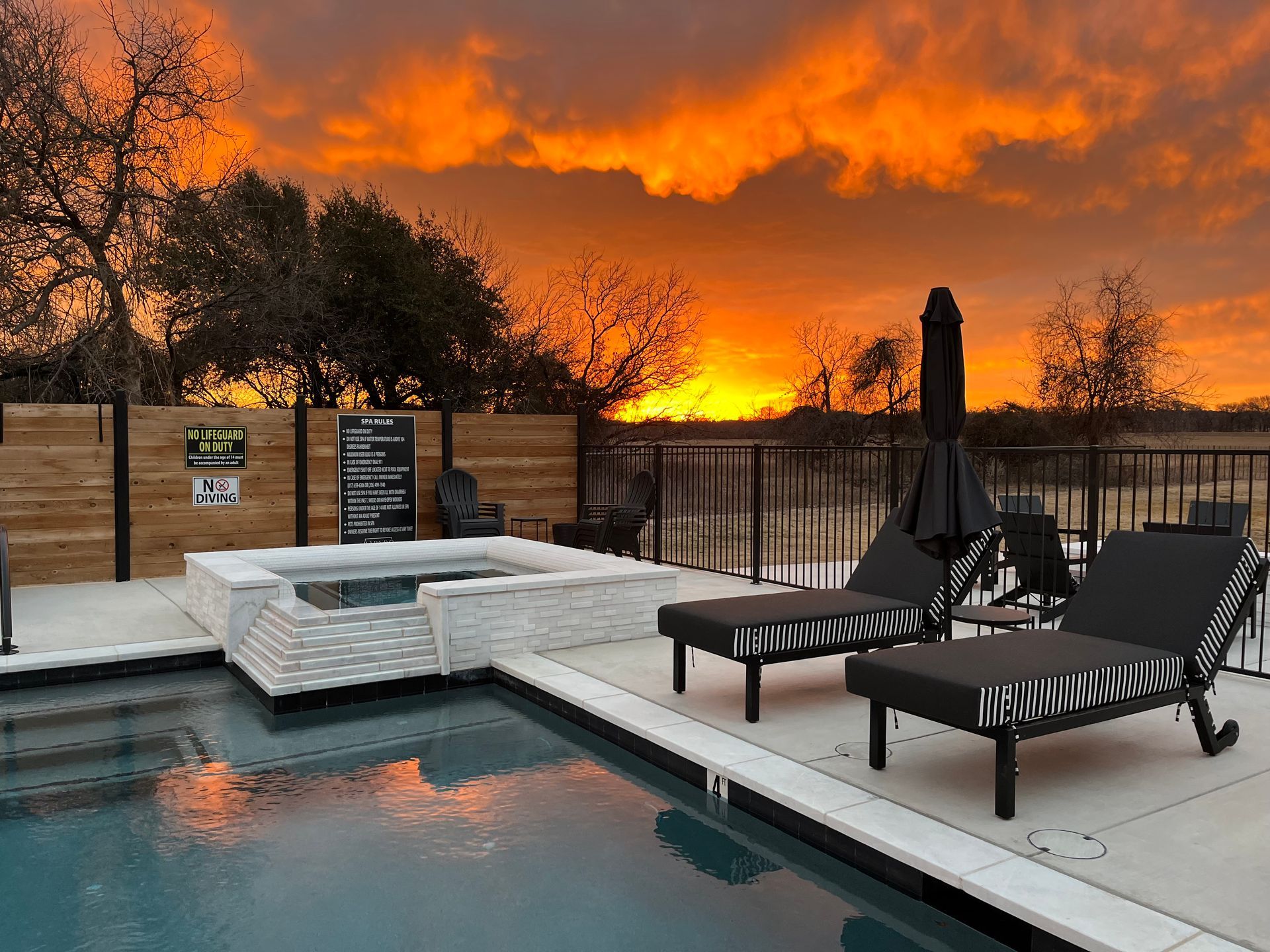 Backyard pool patio with lounge chairs and a fire-lit orange sky in the background