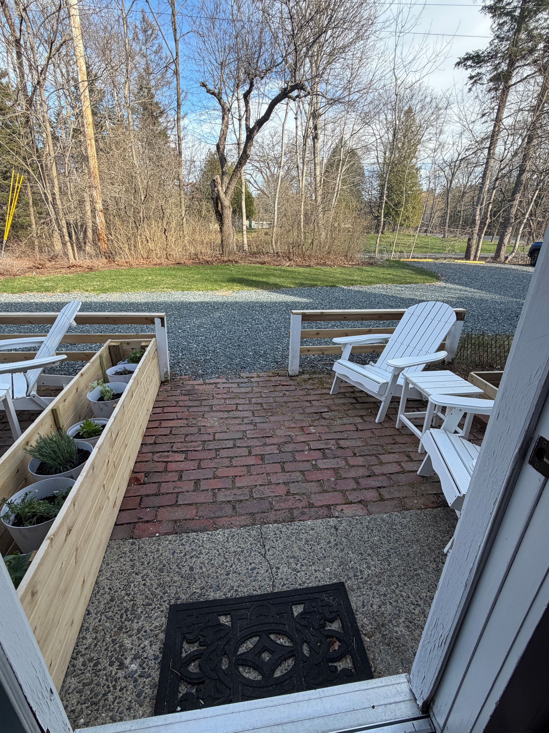 Brick patio with white chairs, gravel, and winter trees beyond a low cedar garden fence.