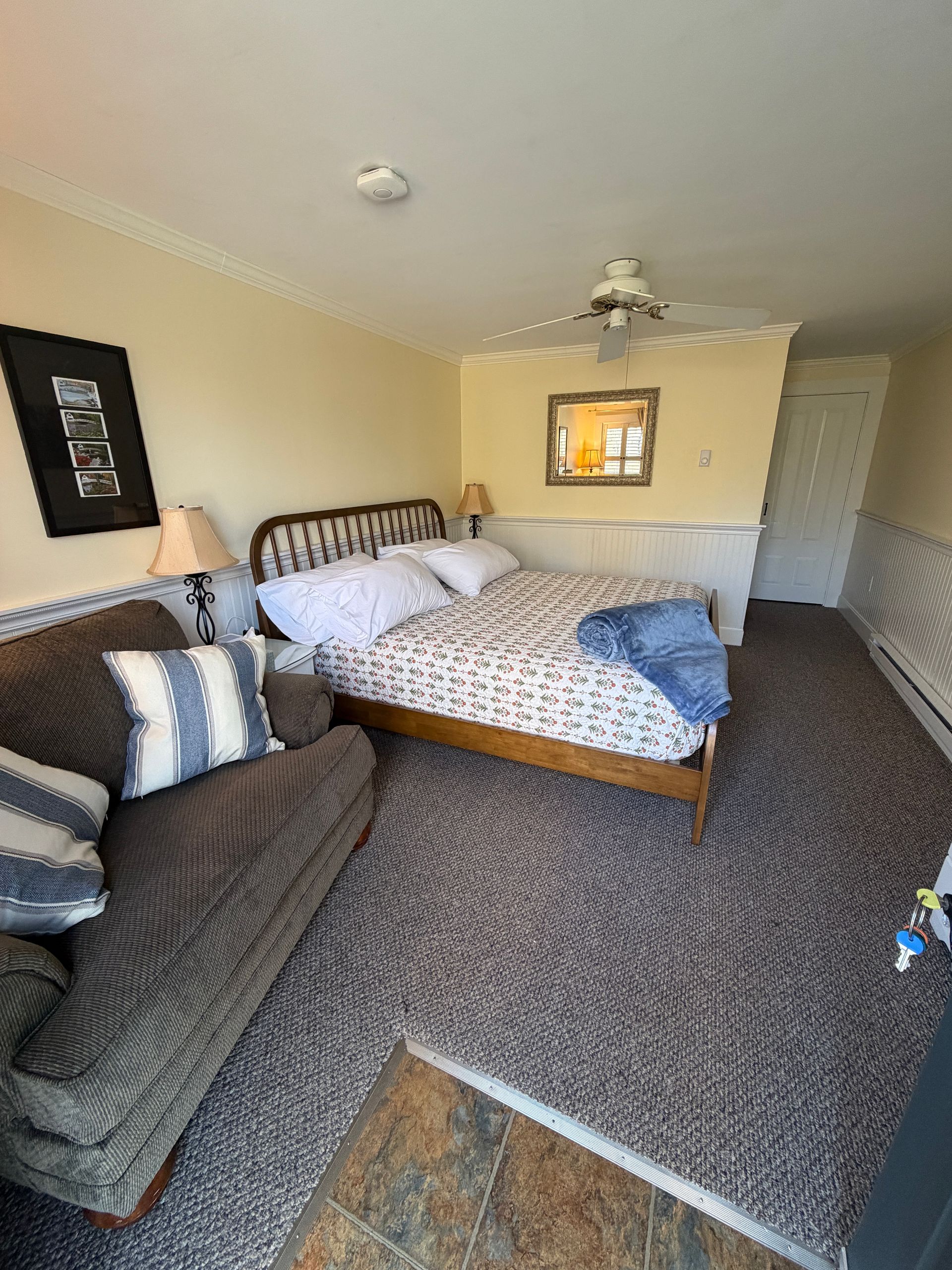 Cozy bedroom with a king bed, sofa, carpet, and framed wall art in yellow and beige tones.