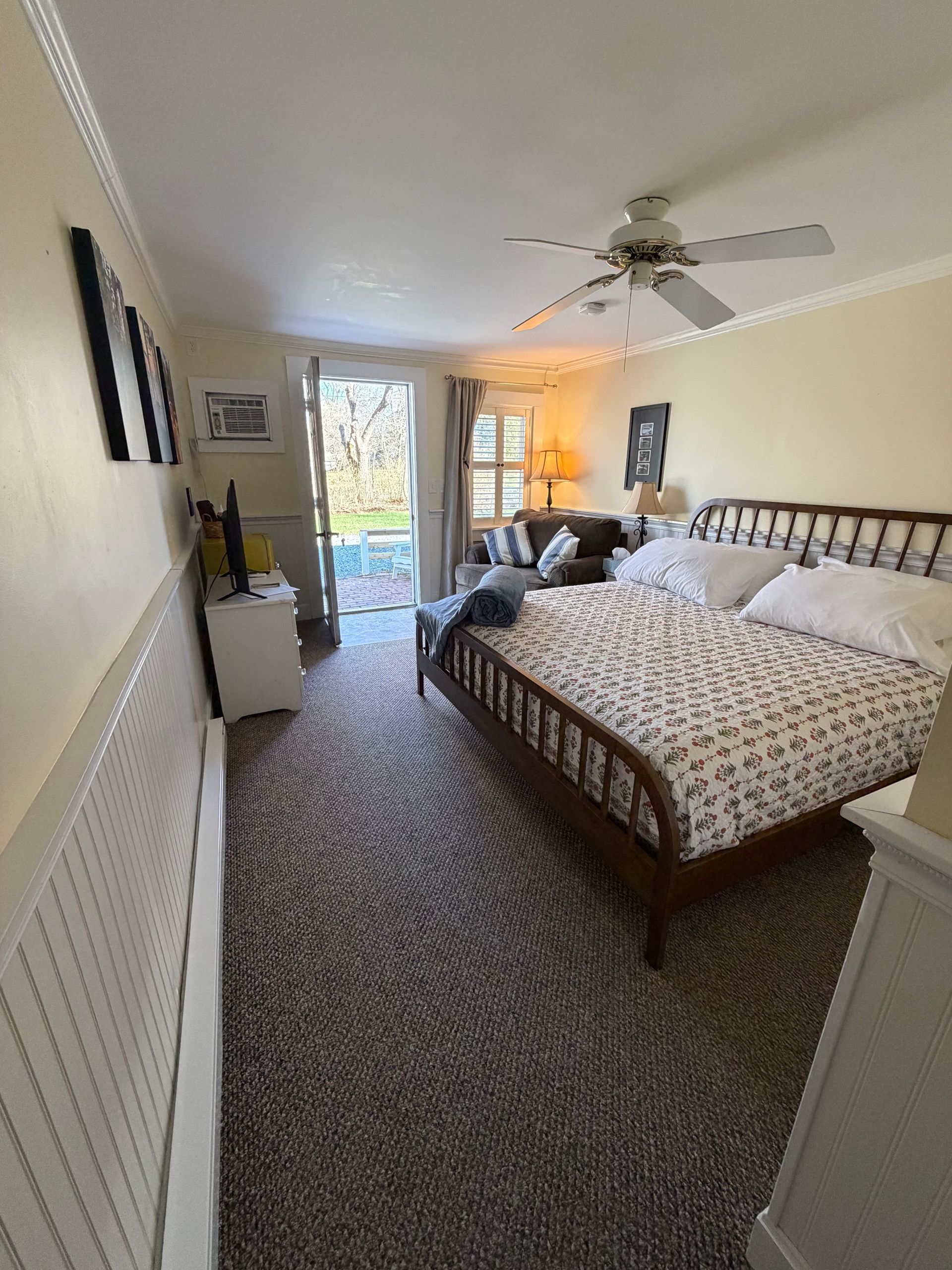 Bedroom with a queen bed, loveseat, and door to a patio. Beige walls, neutral colors.