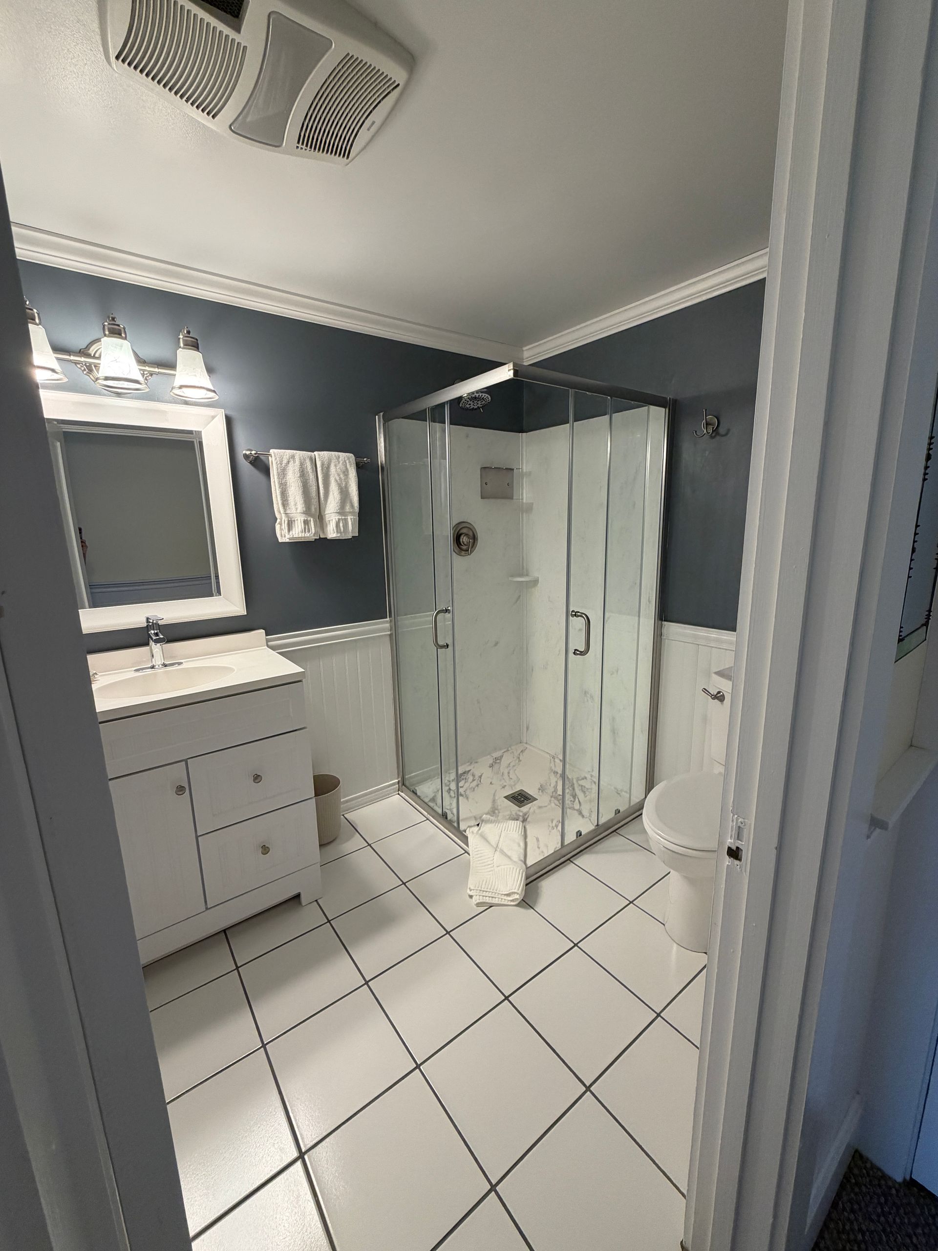 Modern bathroom with white tile, glass shower, vanity mirror, and dark blue walls.