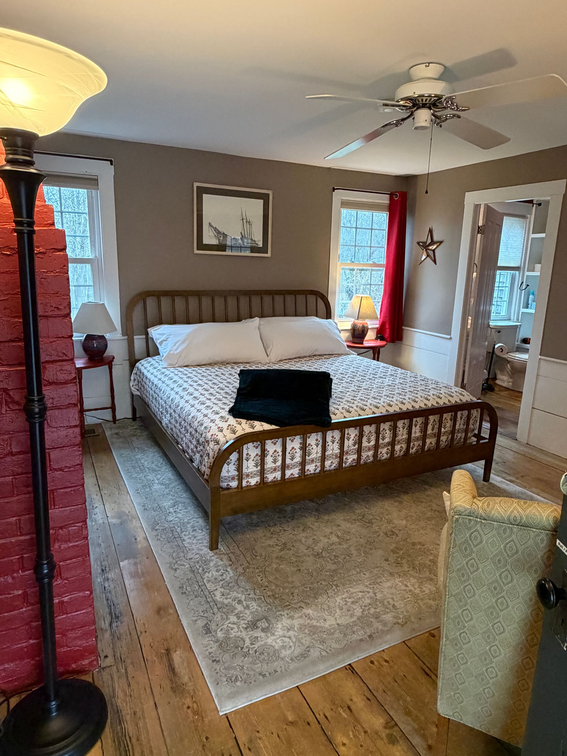 Cozy bedroom with wood bed, gray rug, ceiling fan, and windows letting in daylight