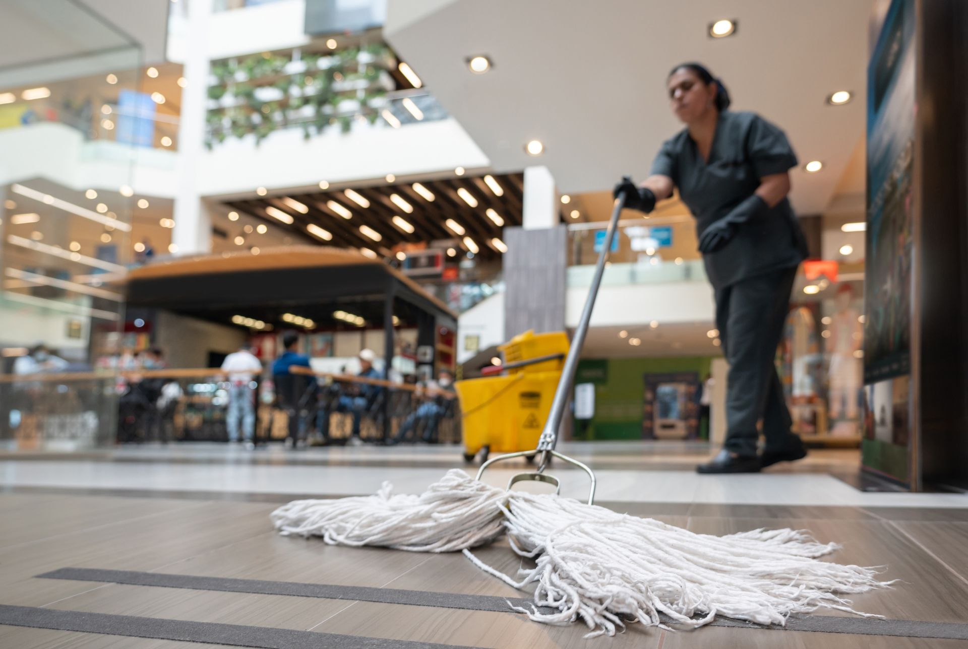 A woman is cleaning the floor of a mall with a mop.