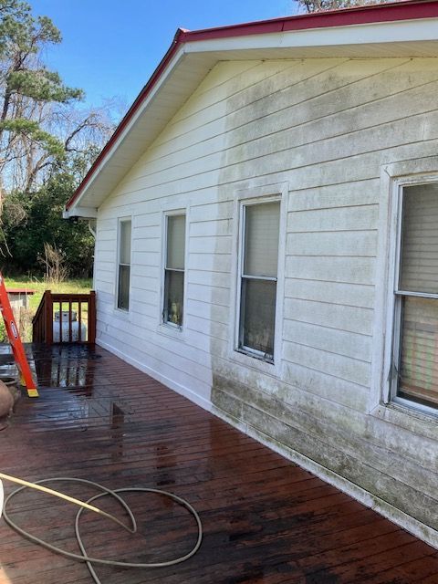 Pressure washer cleaning moldy white siding next to a window.