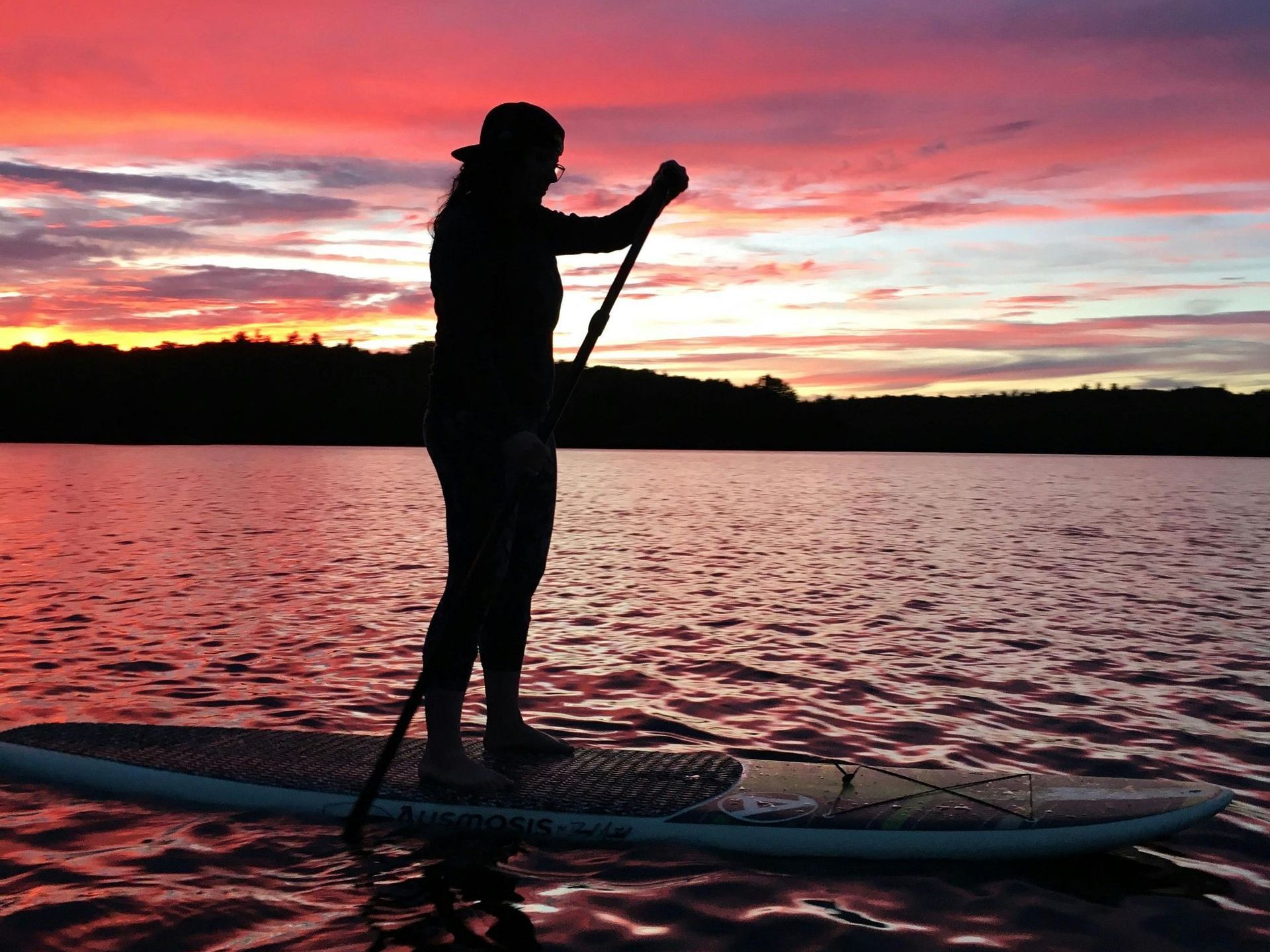 A person is standing on a paddle board in the water at sunset.