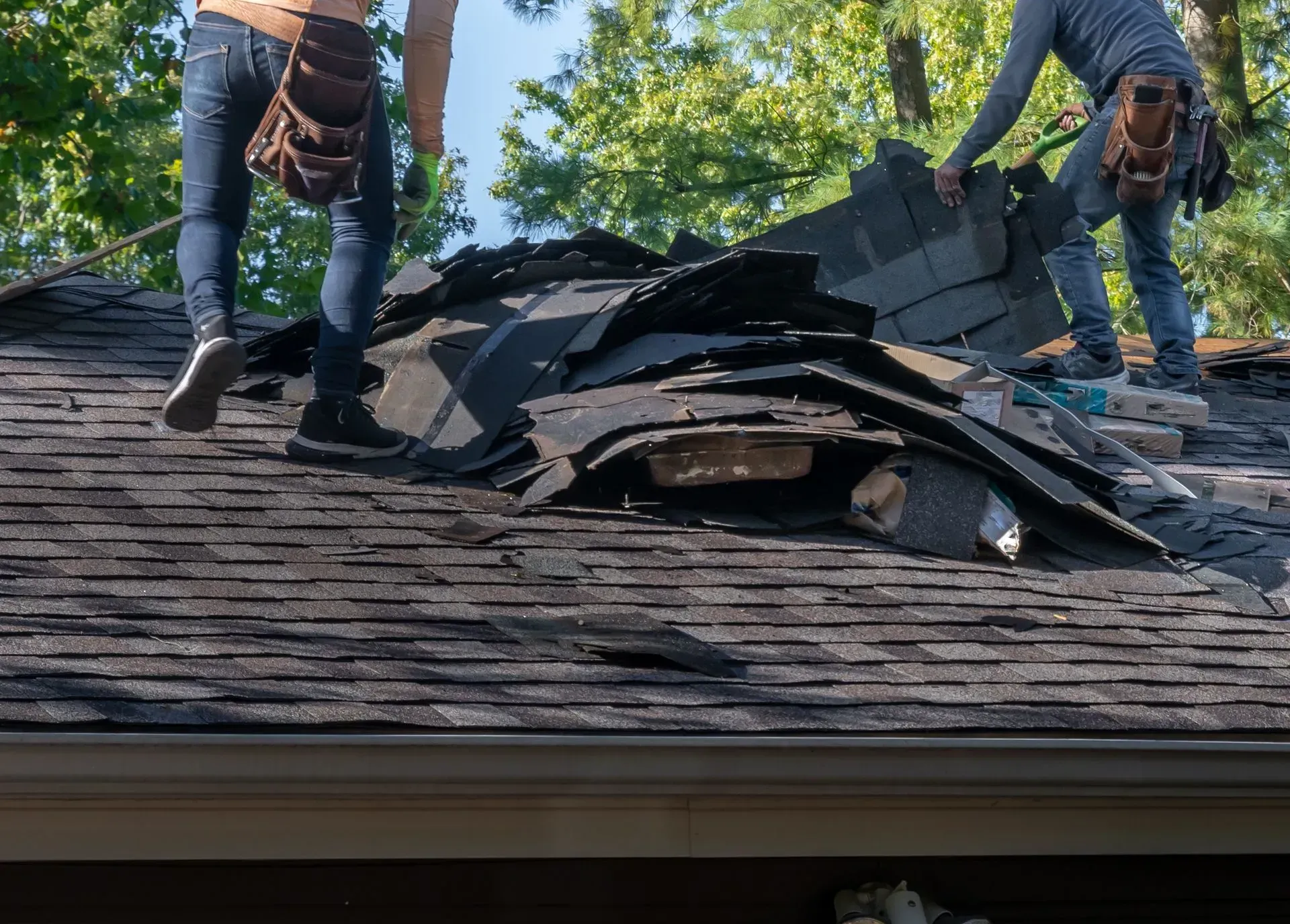 Two workers standing on a damaged roof with torn shingles and exposed underlayment