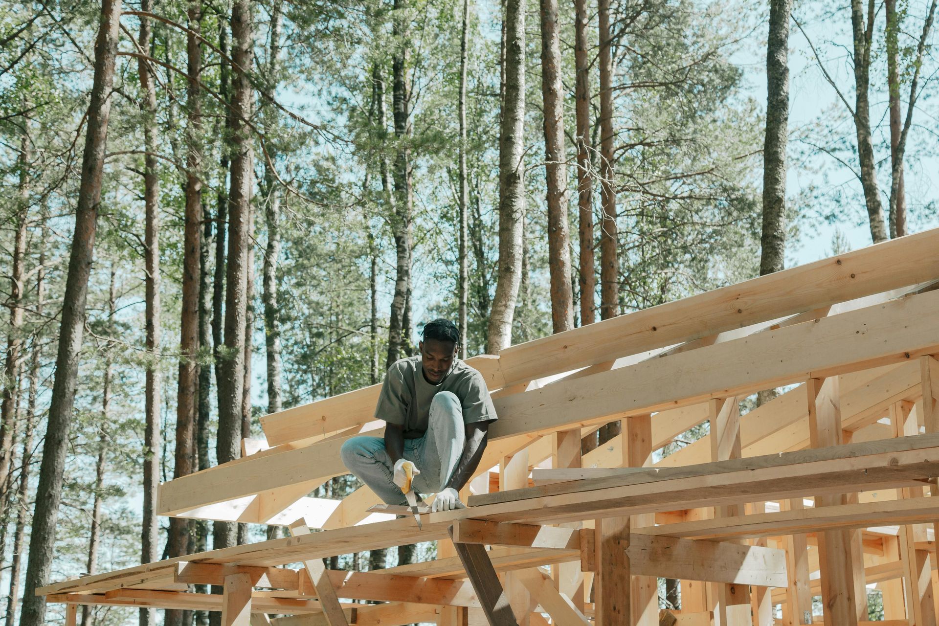 Worker sitting on wooden roof frame at a forest construction site