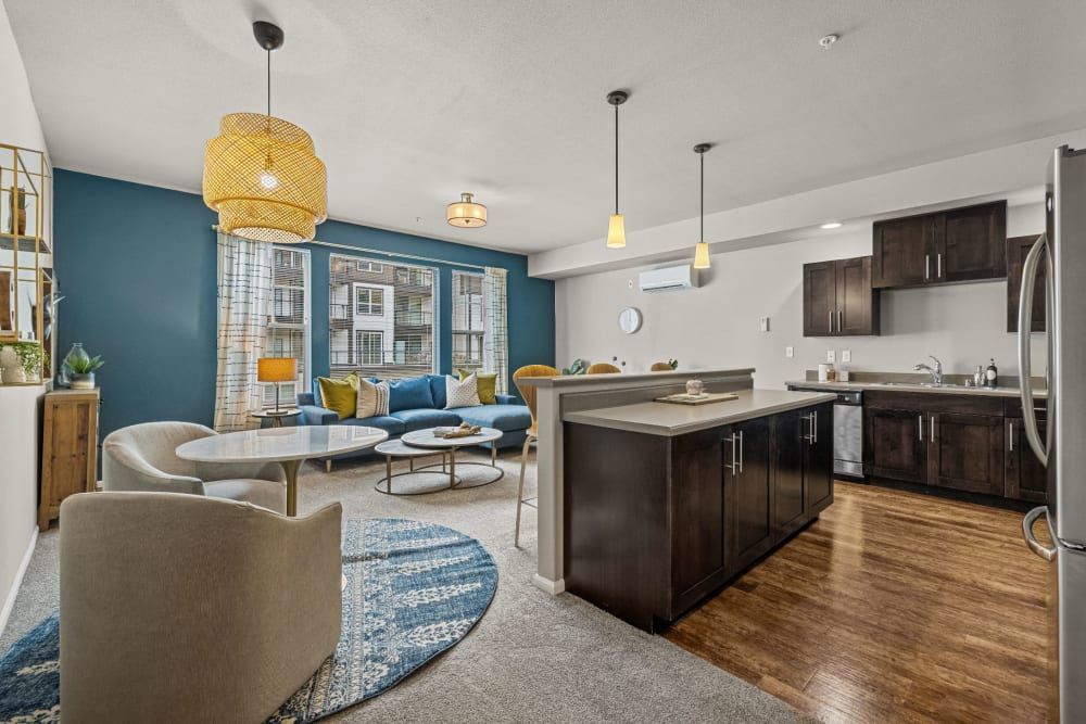 Modern open-concept living space with a combined living and dining area featuring a teal accent wall, stylish hanging lights, and contemporary furnishings, adjacent to a kitchen with dark wood cabinetry and stainless steel appliances at Copperline at Point Ruston in Tacoma, WA.