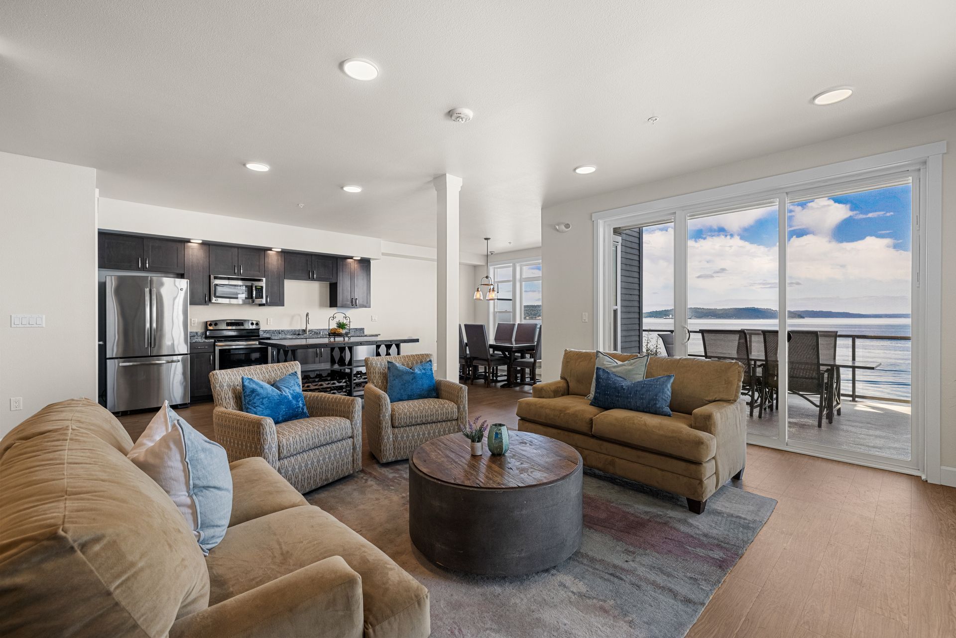 Bright open-concept resident lounge with tan sofas, coffee table, kitchen, and balcony ocean view at Copperline at Point Ruston in Tacoma, WA.