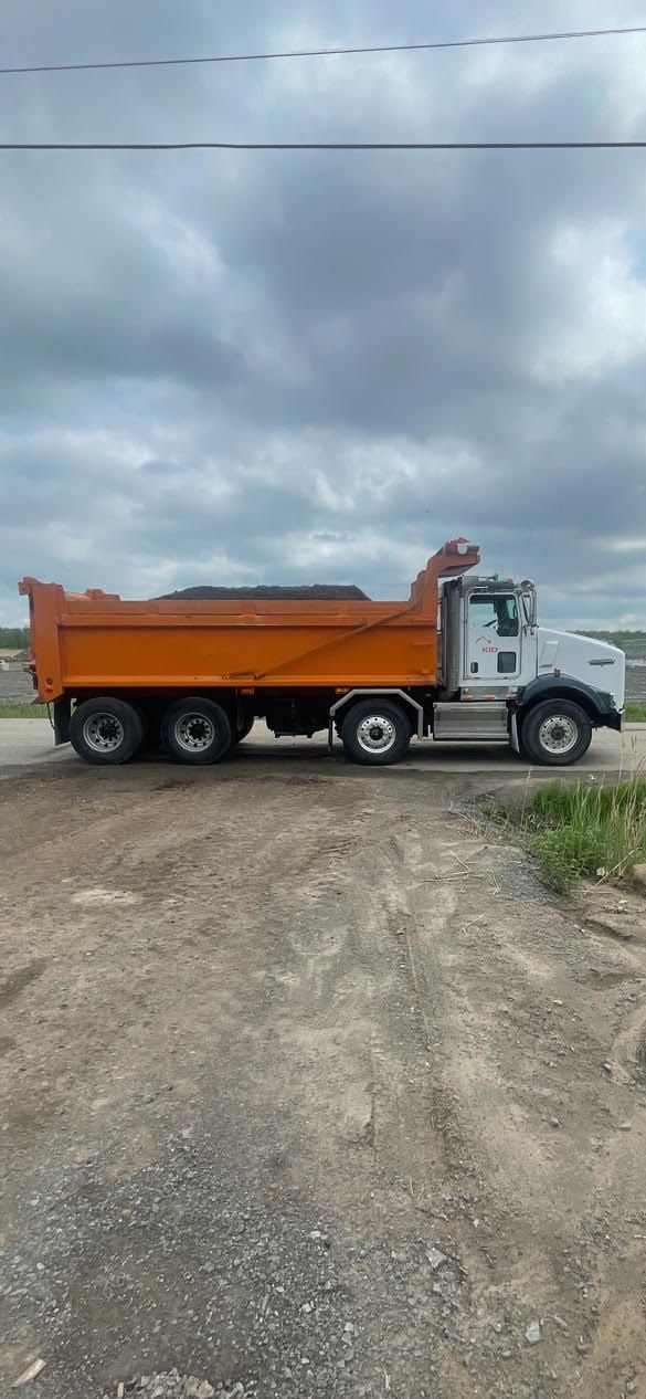 Un camion à benne basculante est garé sur le bord d'un chemin de terre.