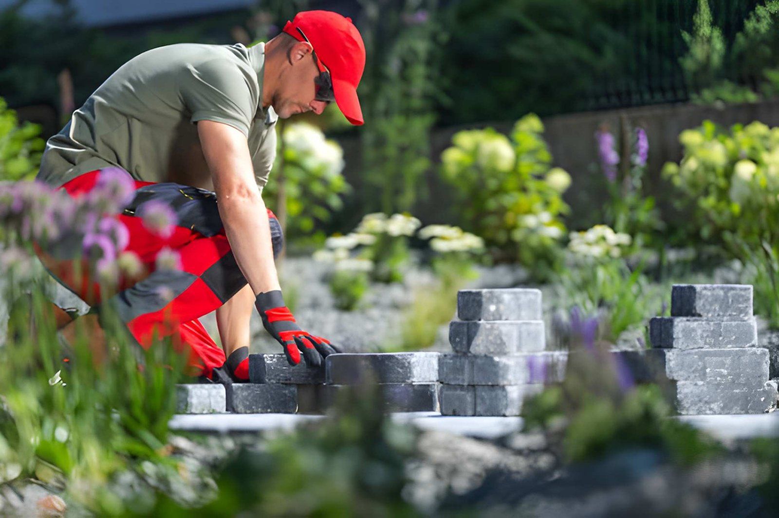 Worker in red cap stacking gray paving stones in a garden bed
