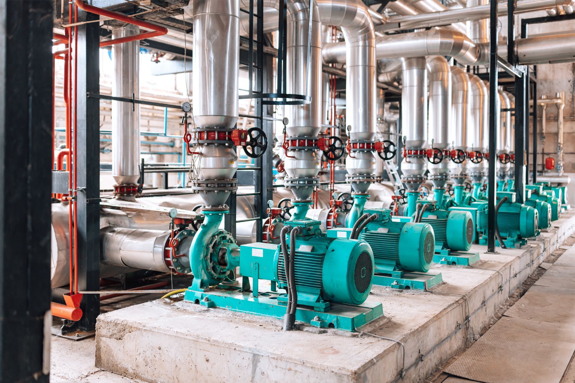 A row of green pumps and pipes in a factory.